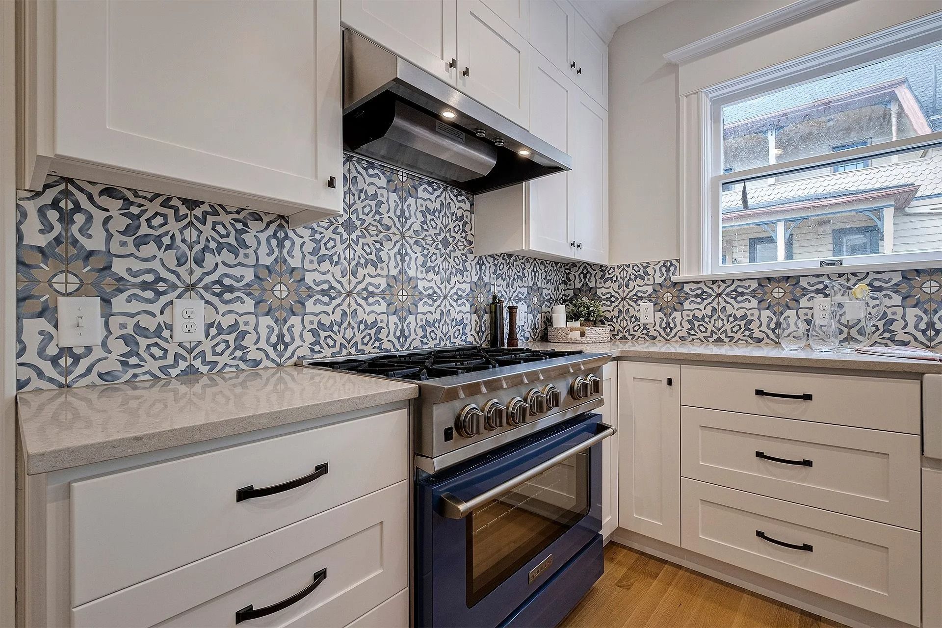 Kitchen with white cabinets, blue oven, patterned backsplash, and window.