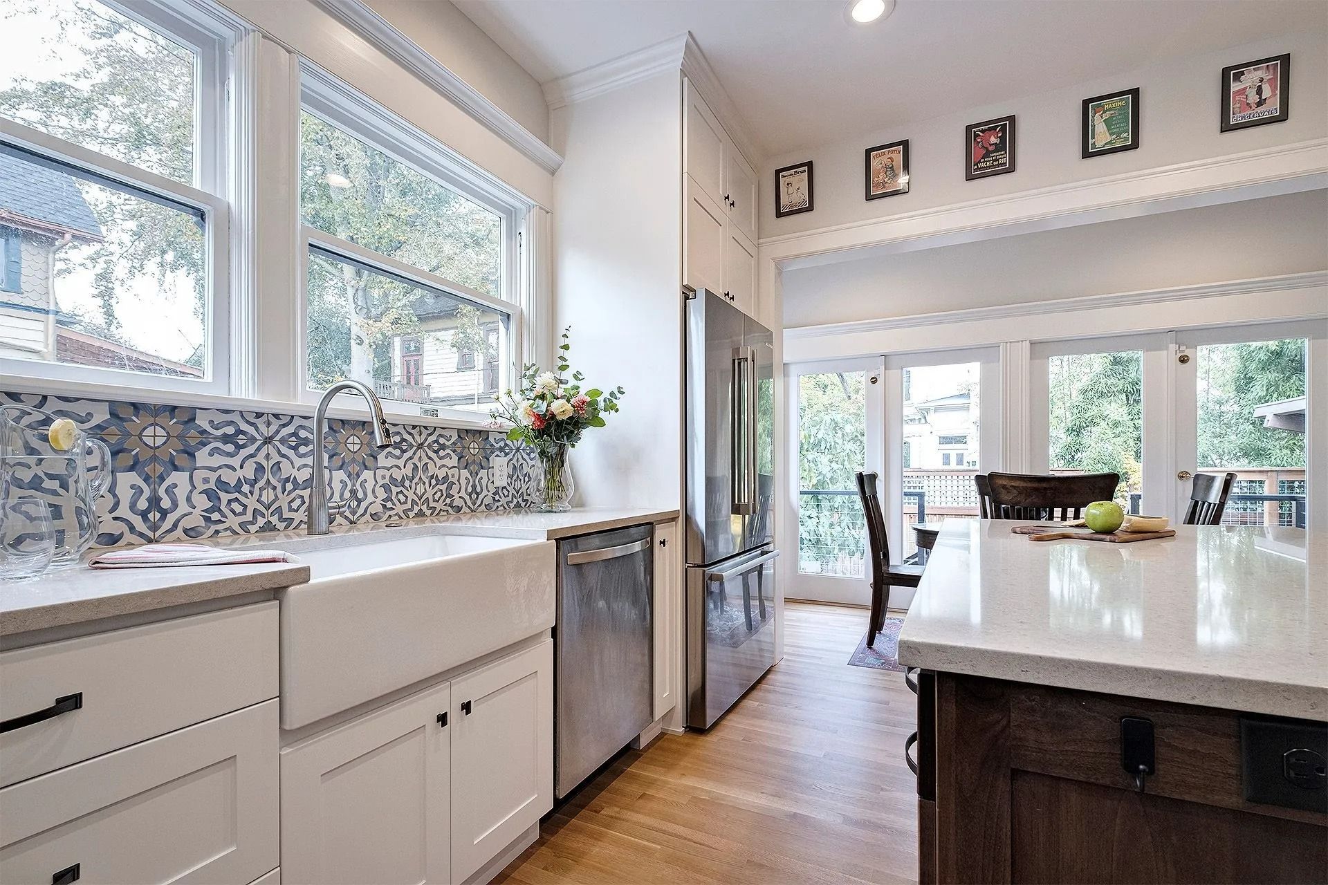 Bright kitchen with white cabinets, farmhouse sink, patterned backsplash, stainless steel appliances, and large windows.