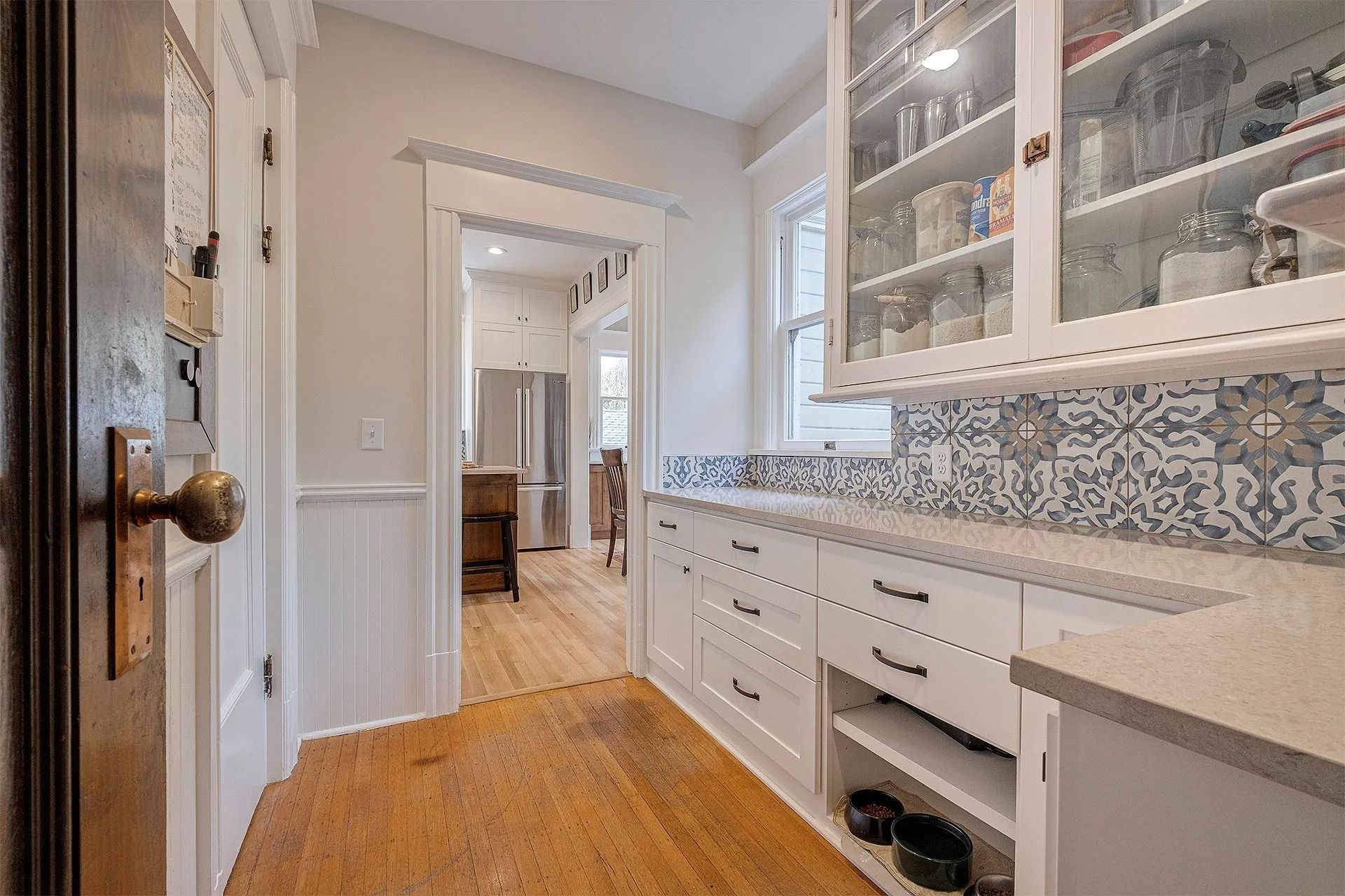 Hallway with white cabinets, patterned backsplash, and wooden floors. Door on the left.