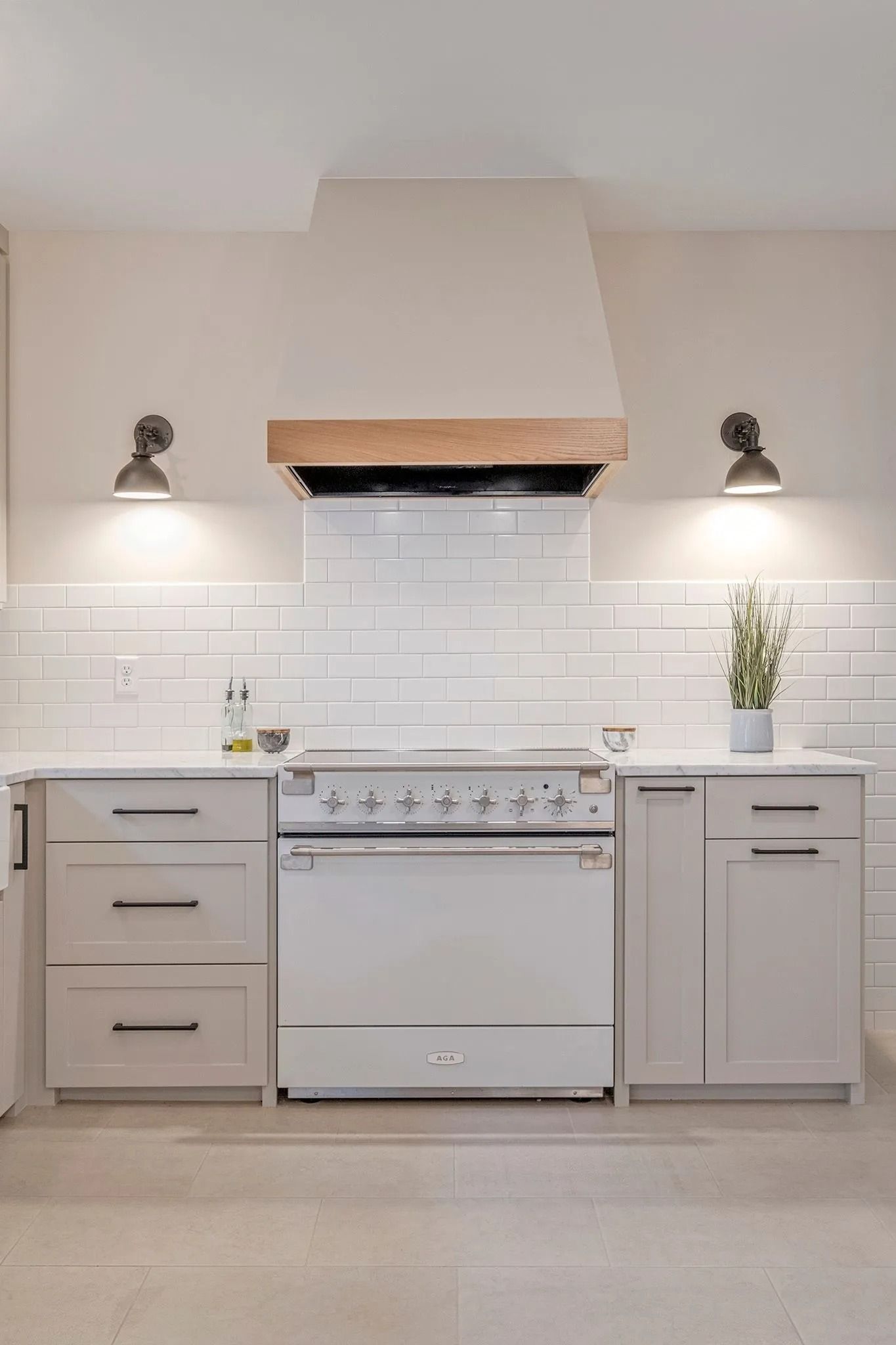 Kitchen with white cabinets, stove, and light-colored backsplash, under a wooden range hood.