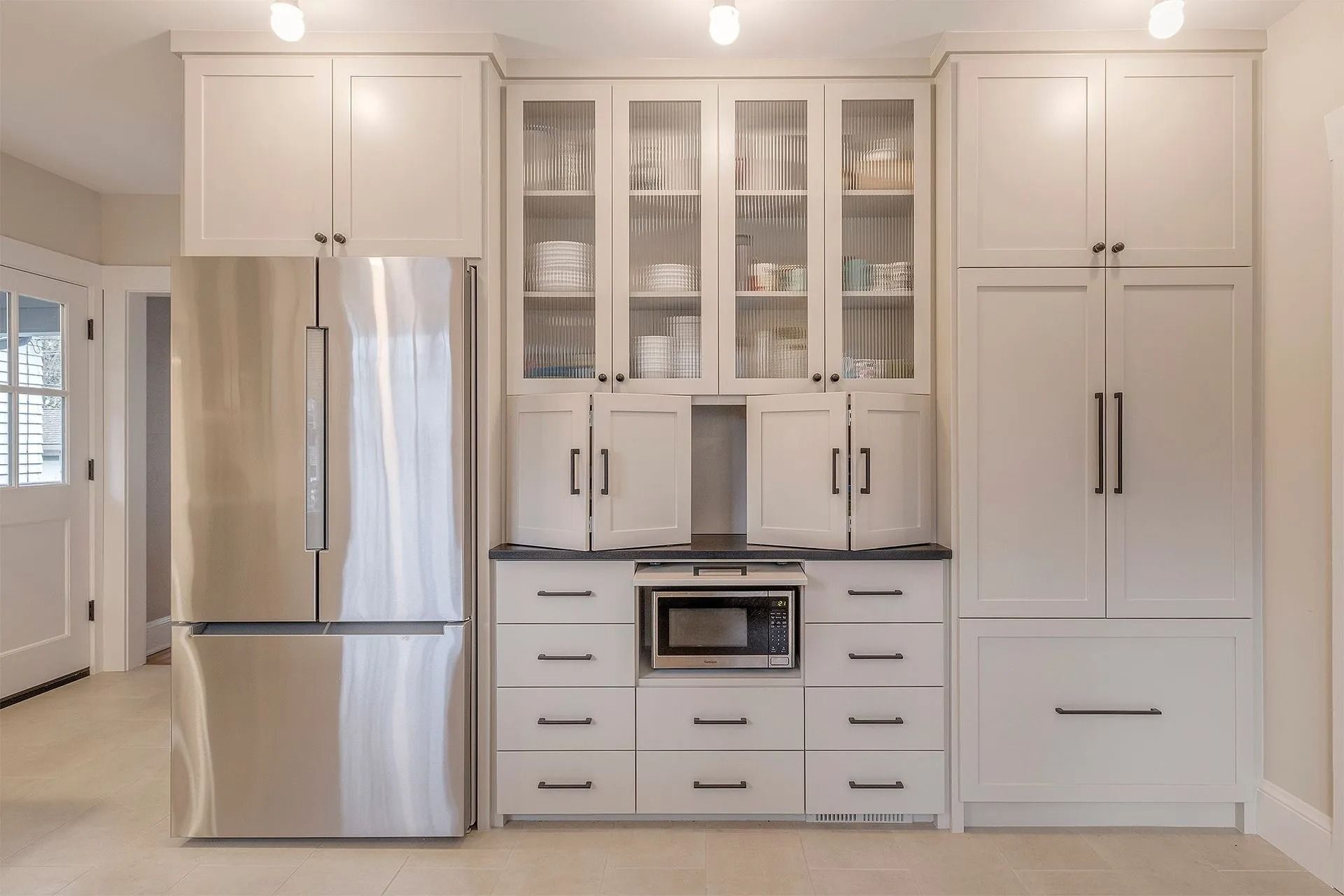 White kitchen cabinets with stainless steel refrigerator, microwave, and glass-front display cabinets.