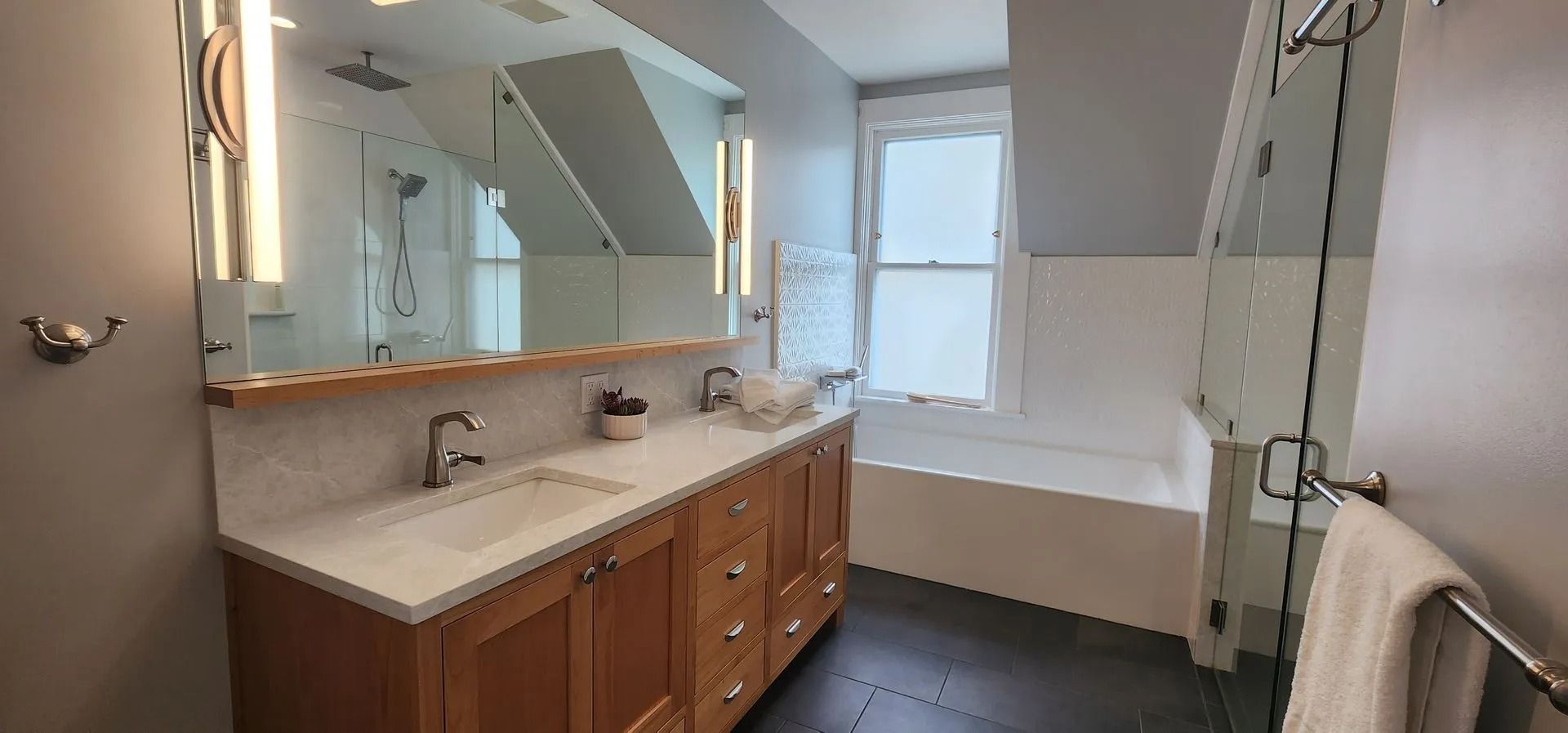 Bathroom with double vanity, mirror, tub, and window in a renovated space.