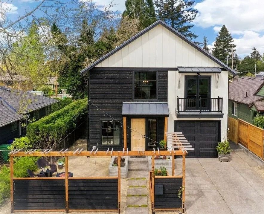 Modern two-story house with black siding, white upper level, and a wooden patio area.
