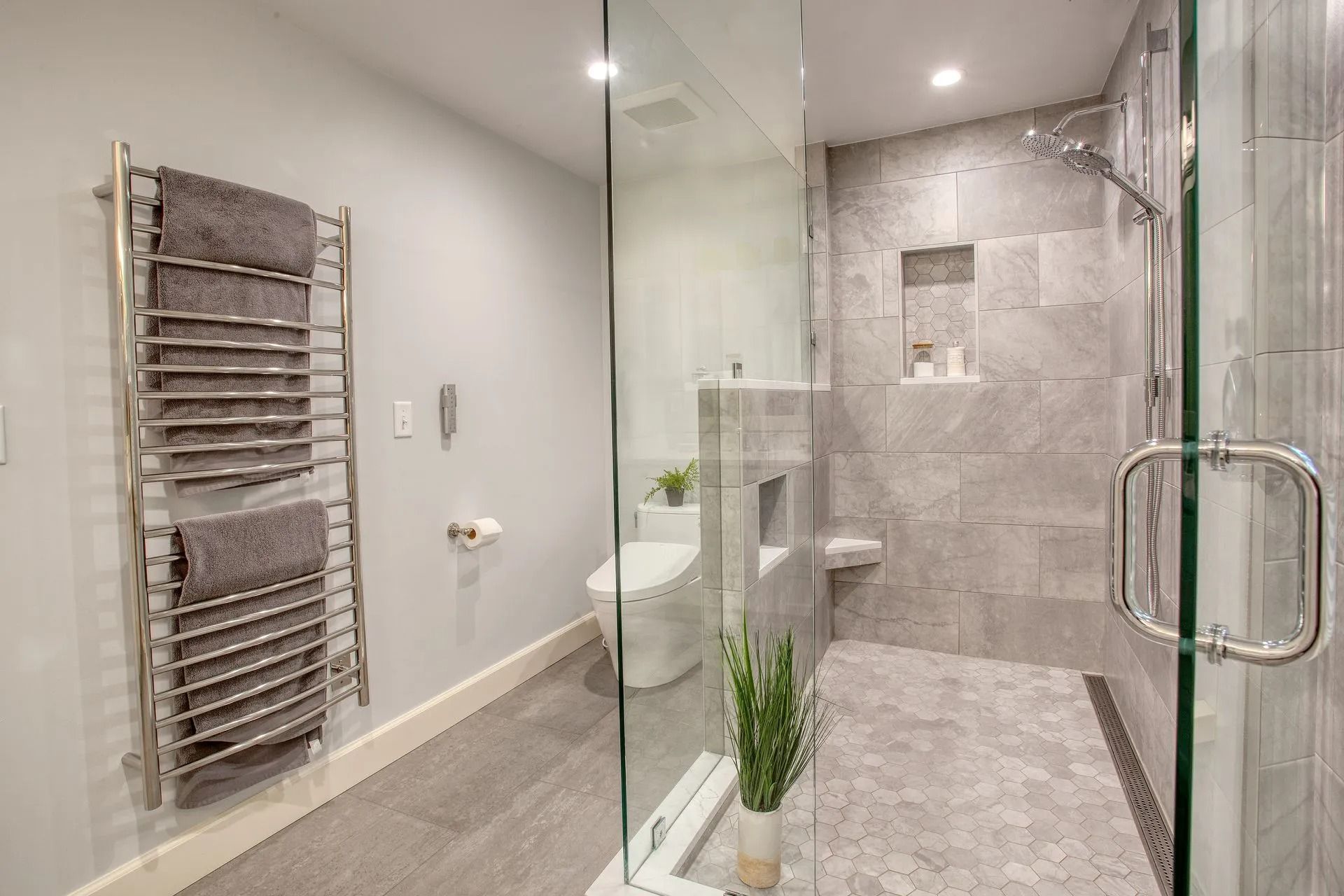 Modern bathroom with glass shower, heated towel rack, and gray tile.