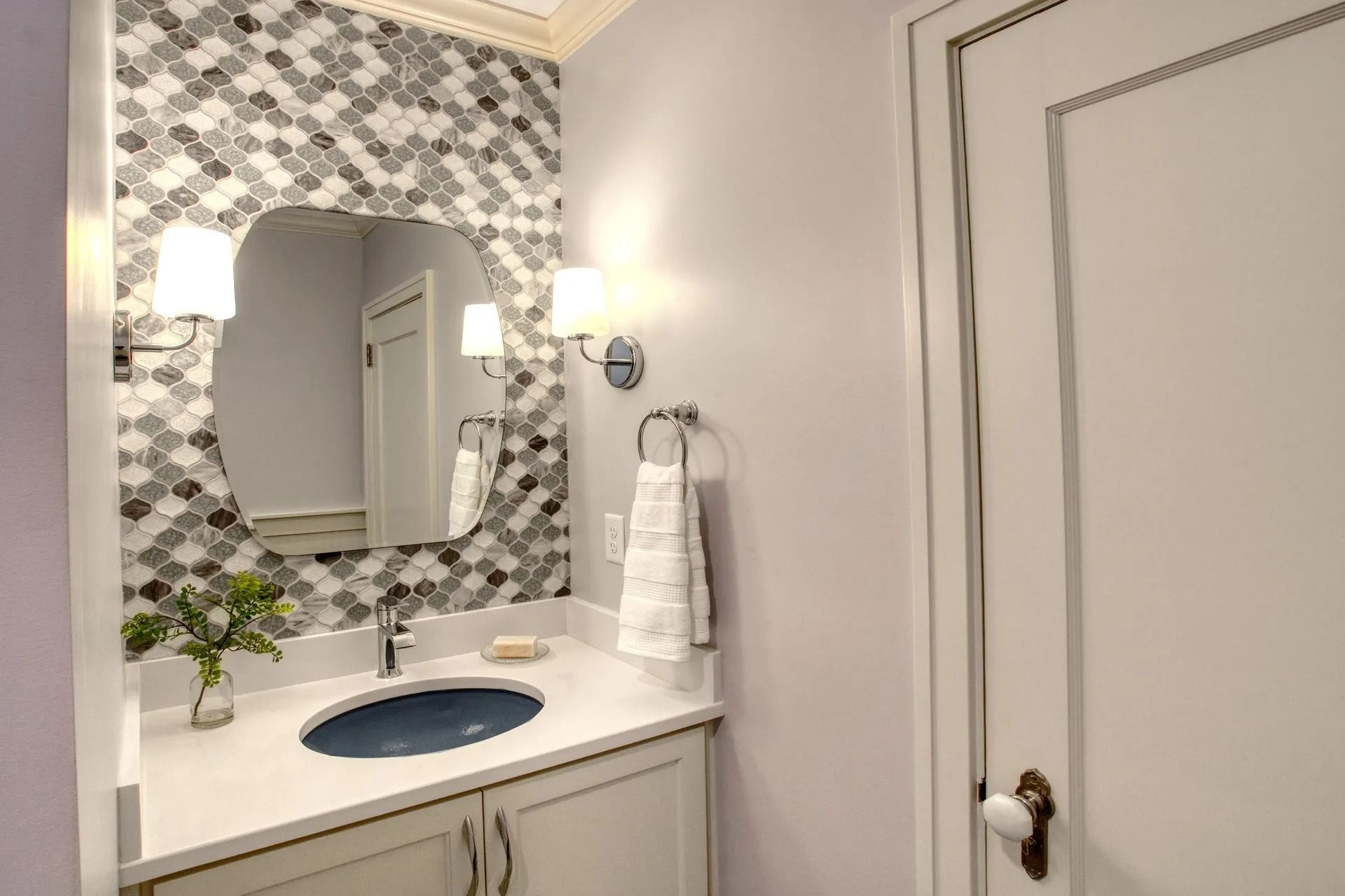 Powder room with decorative tile backsplash, scalloped mirror, and white vanity.