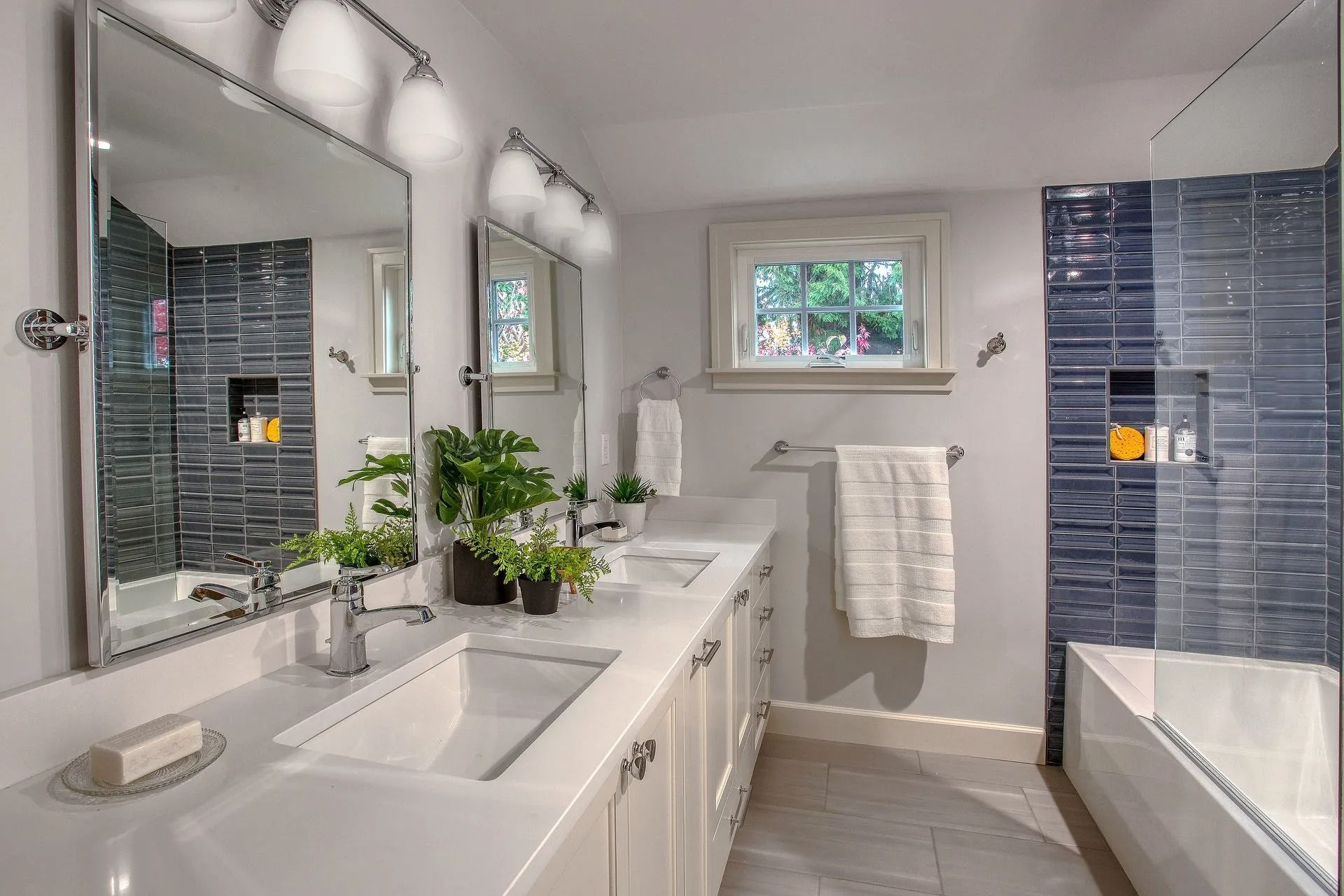 Modern bathroom with white countertops, blue tile shower, and double sinks.