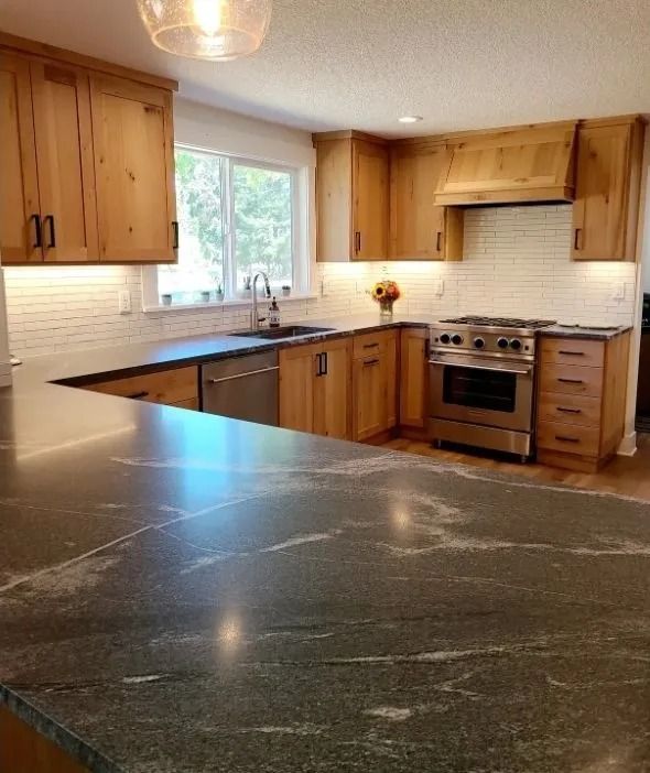 Kitchen with wood cabinets, dark countertops, stainless steel appliances, and white backsplash.