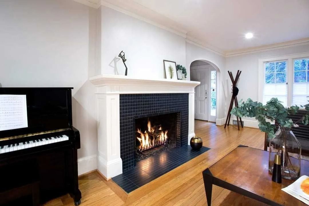 Living room with a fireplace, piano, wooden floors, and a table with plants.