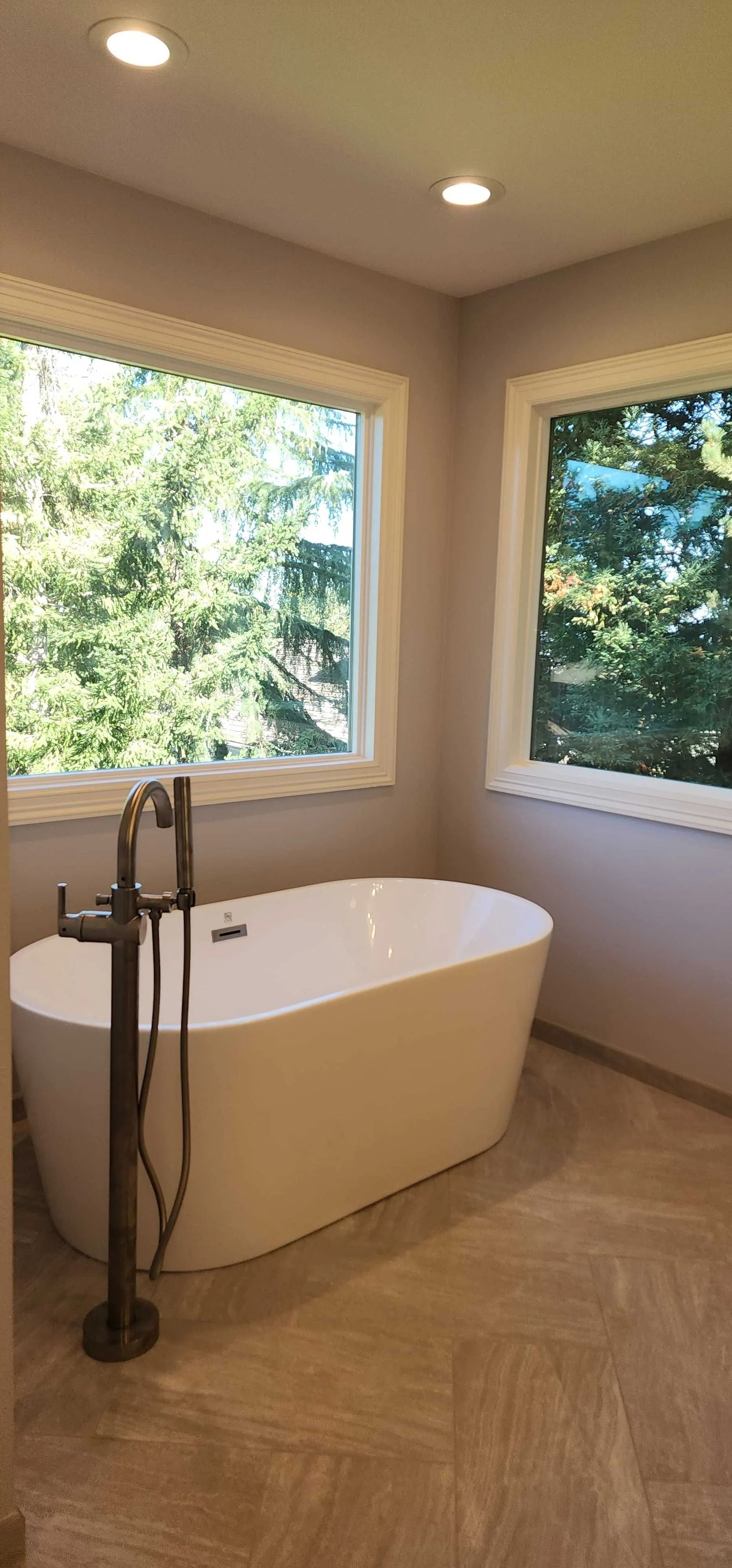 Bathroom with a white freestanding bathtub and a dark faucet fixture by a large window.