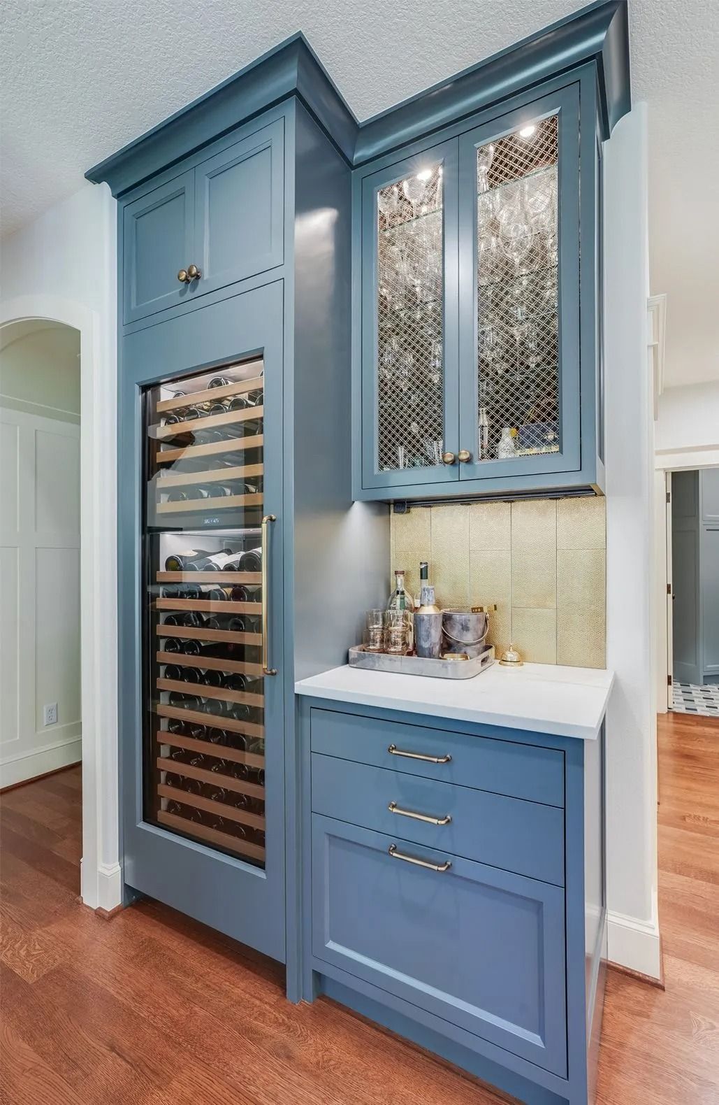 Blue wine cabinet with wine cooler, glass-front cabinet, drawers, and counter in a home setting.