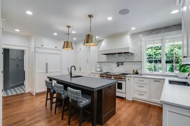 Elegant kitchen with white cabinets, dark island, gold pendant lights, and hardwood floors.