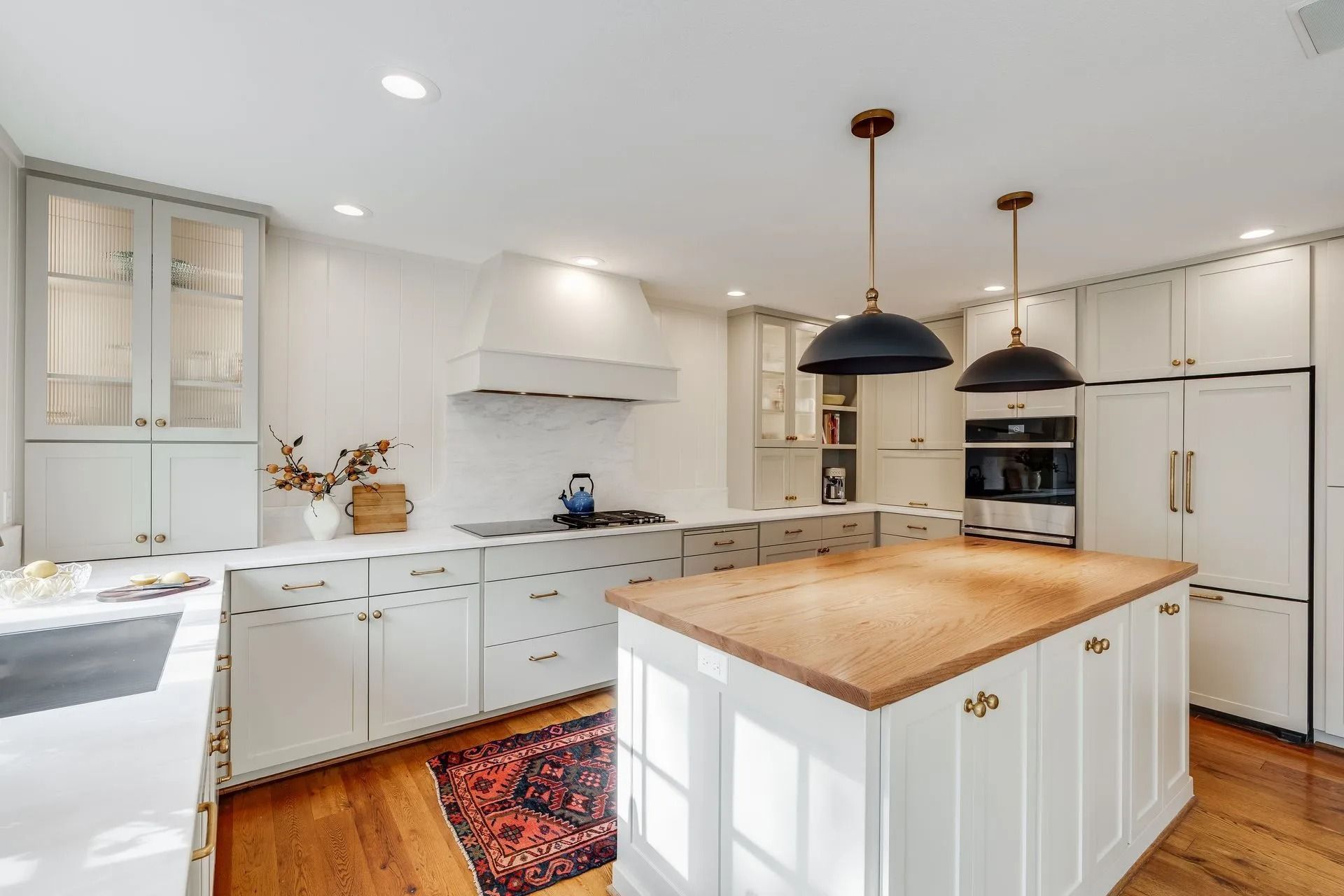 White kitchen with island, wooden countertops, and black pendant lights.