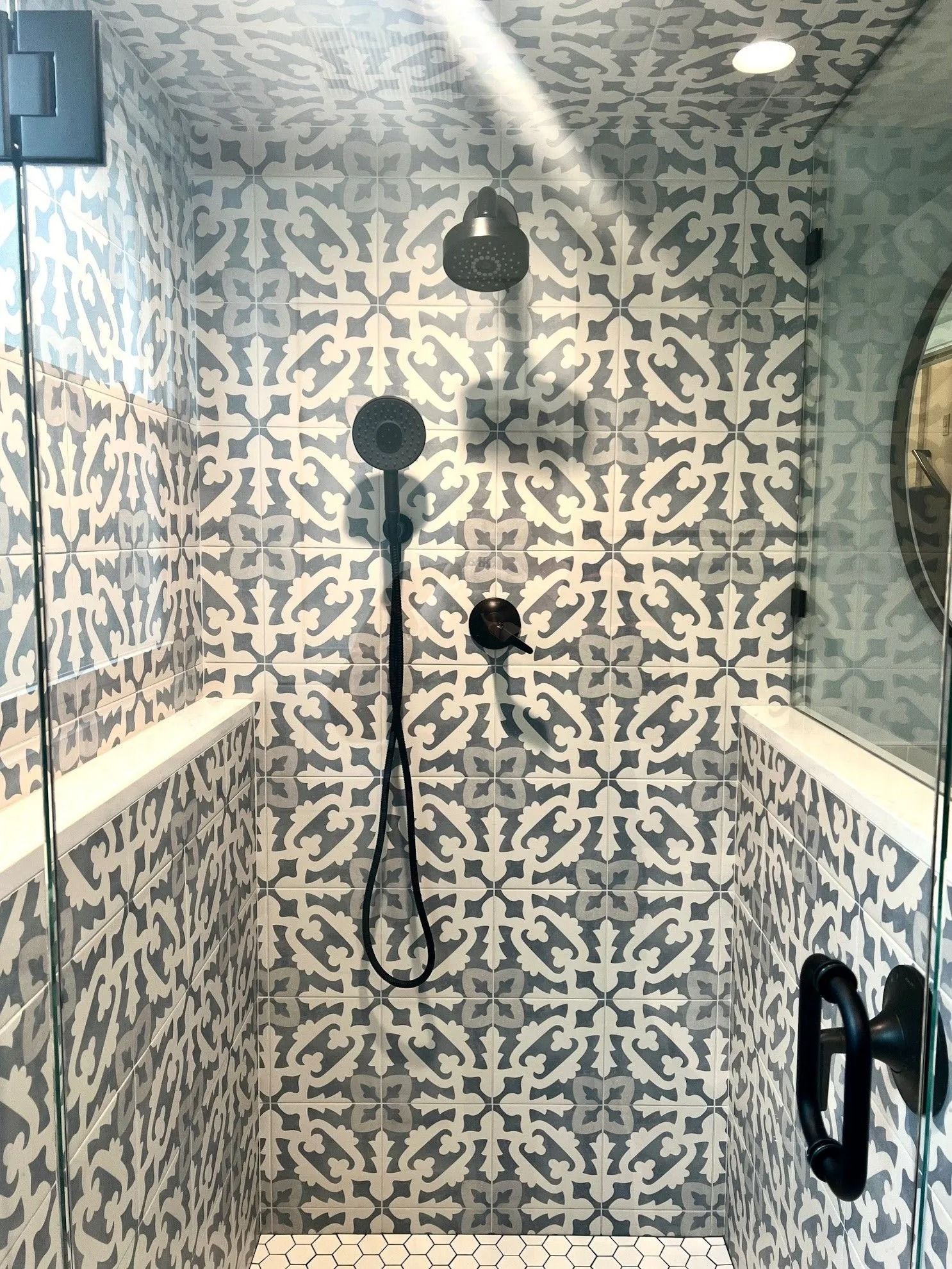 Shower with patterned gray and white tile, black fixtures, and glass doors.