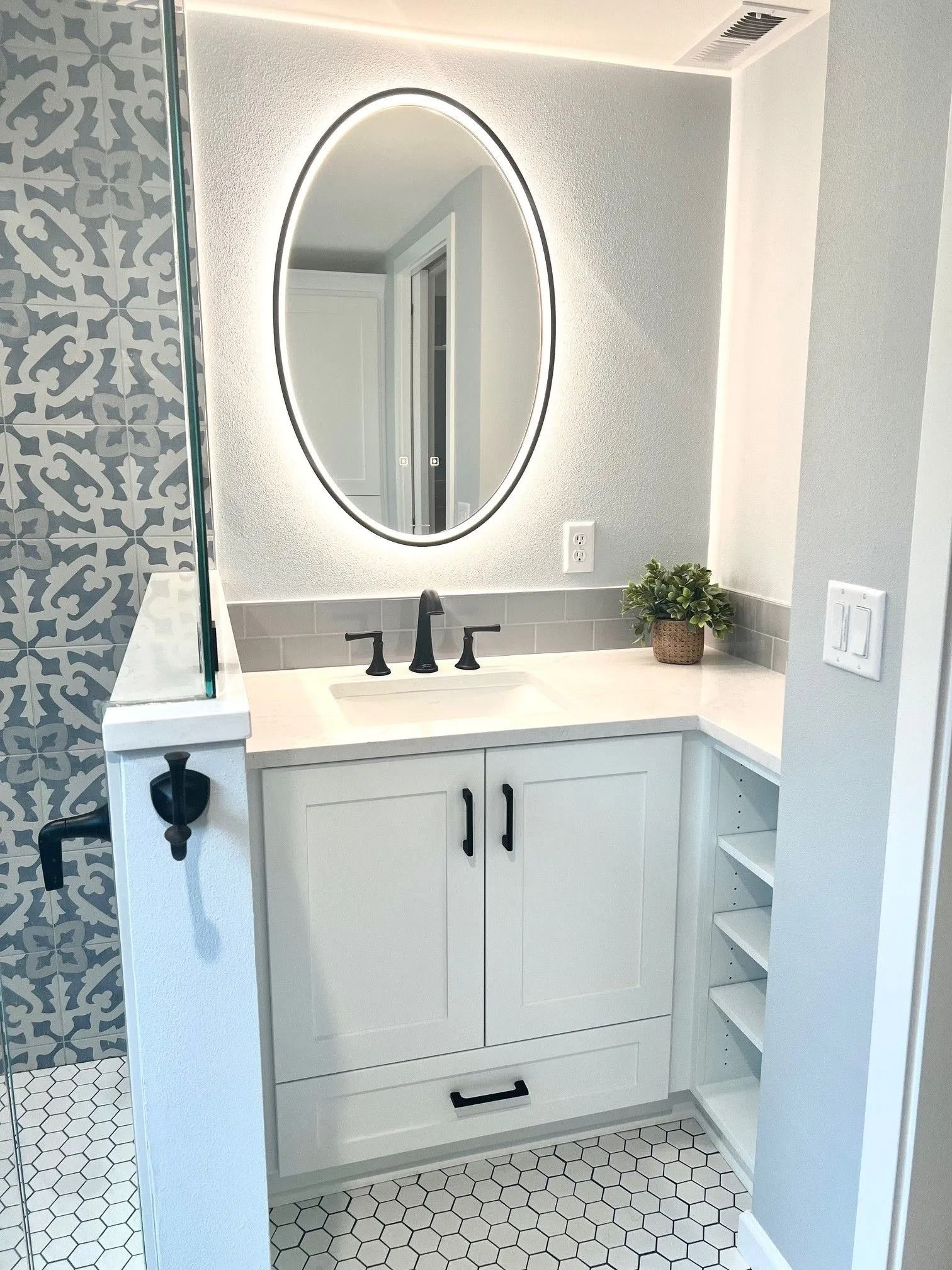 Bathroom with white vanity, oval backlit mirror, black faucet, and patterned tile.
