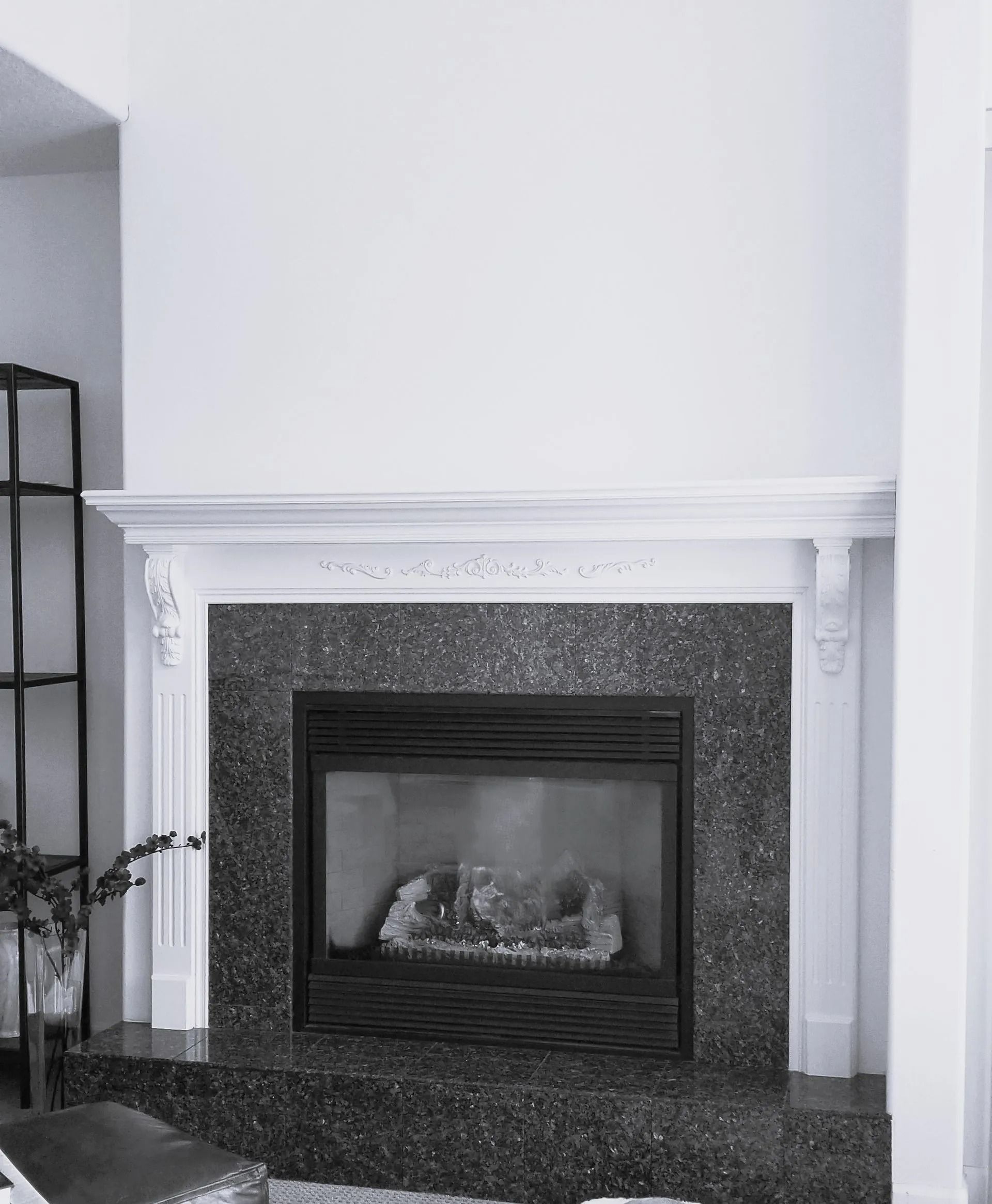 Fireplace with dark speckled surround and white mantel against a white wall.