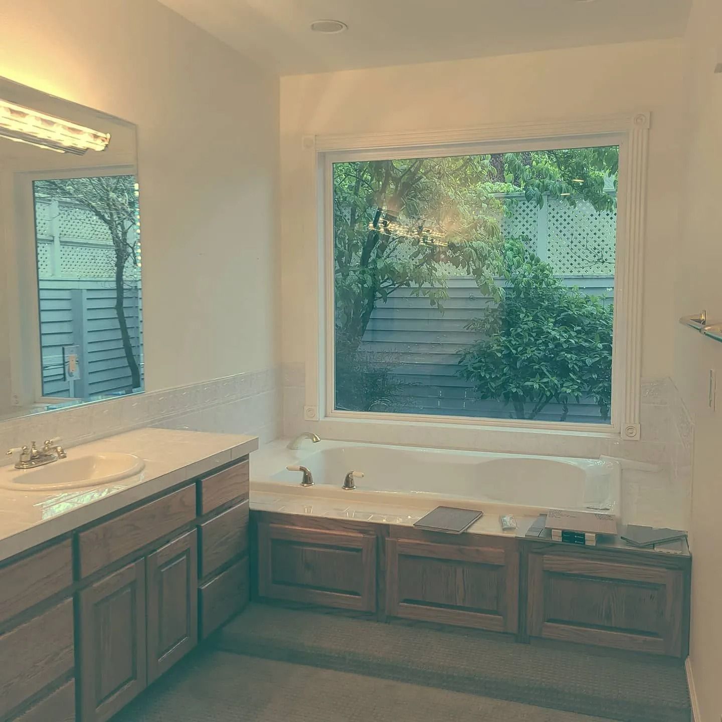 Bathroom with a large window overlooking greenery, a built-in tub, and wood cabinetry.
