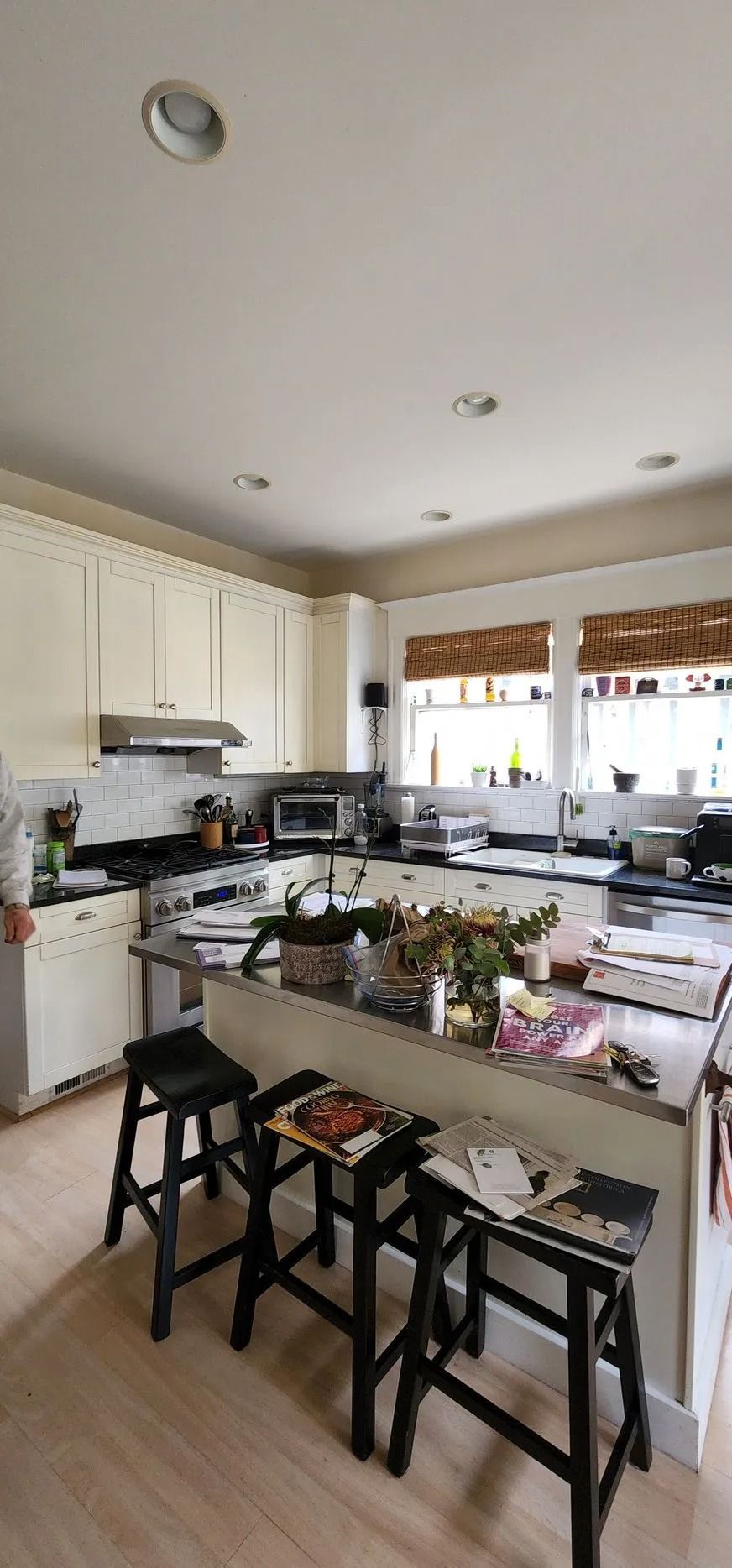 Kitchen with black countertops, light cabinets, and three black stools at an island.