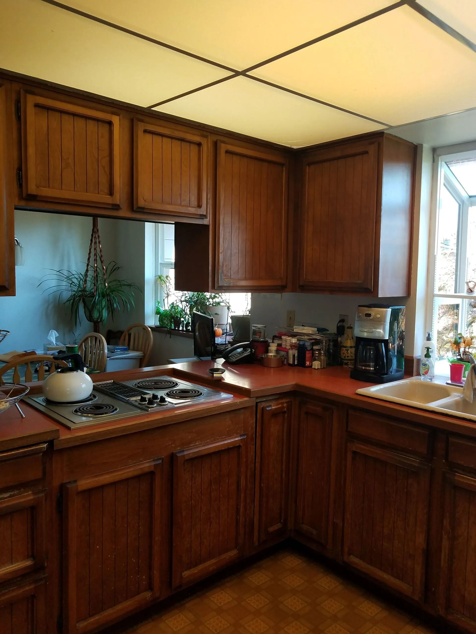 Kitchen with wooden cabinets, reddish countertops, and a white ceiling with a window on the right.