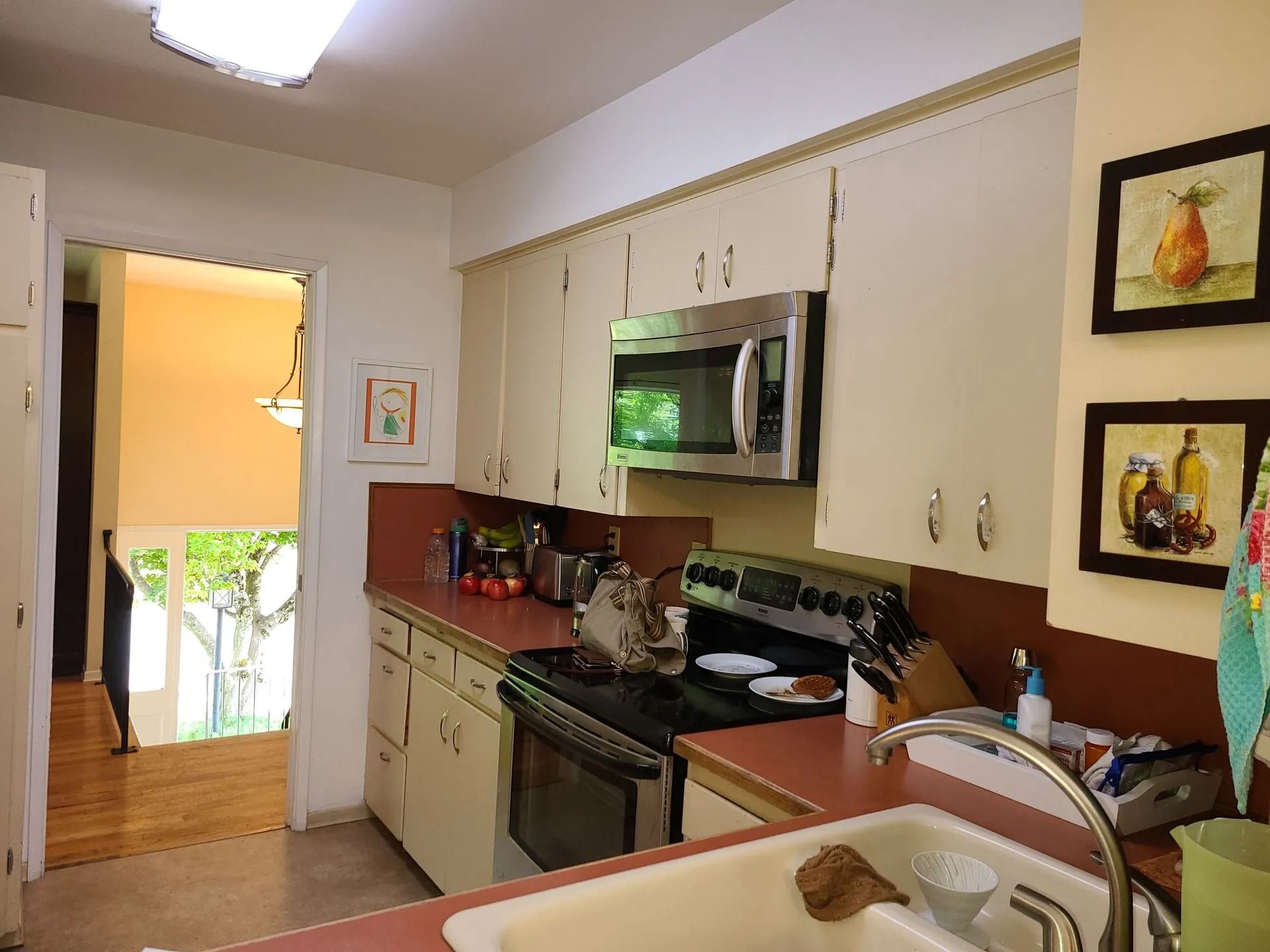 Kitchen with white cabinets, stainless steel microwave, pink counters, and a sink.