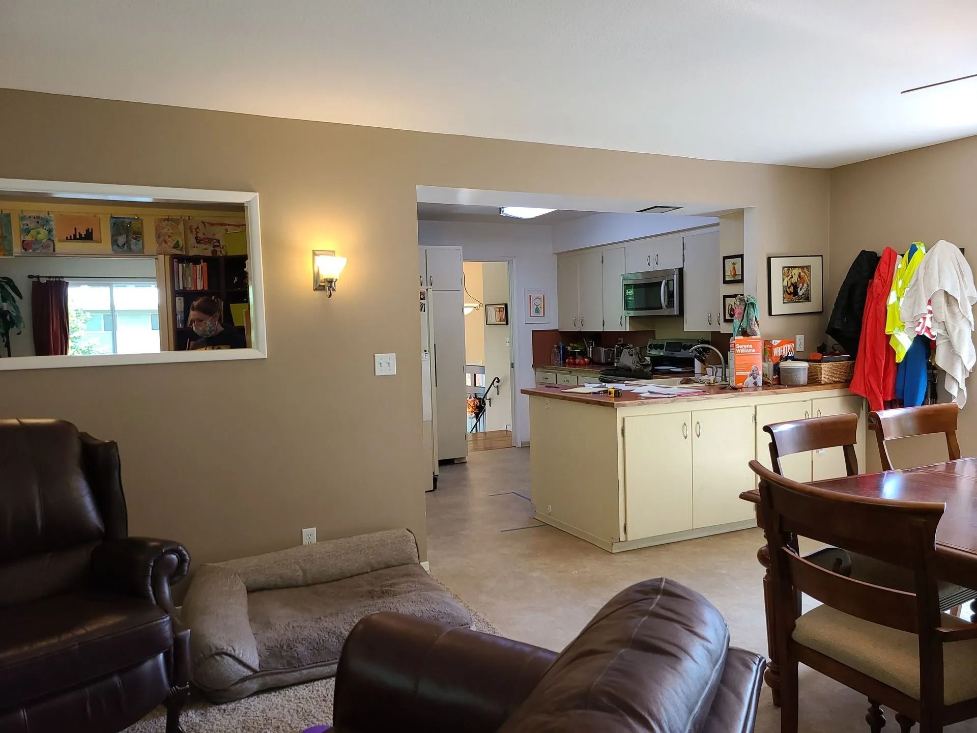 Living room with kitchen in background. Tan walls, brown furniture, beige cabinets, and open doorway.