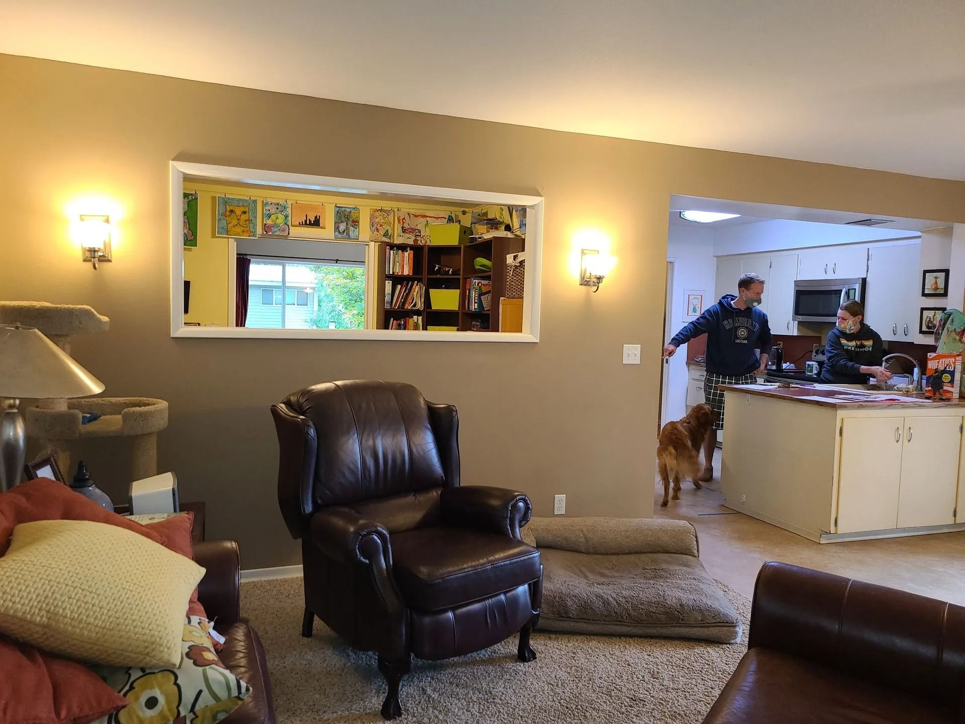 Living room with brown leather chair, mirror reflecting kitchen, people, and a dog.