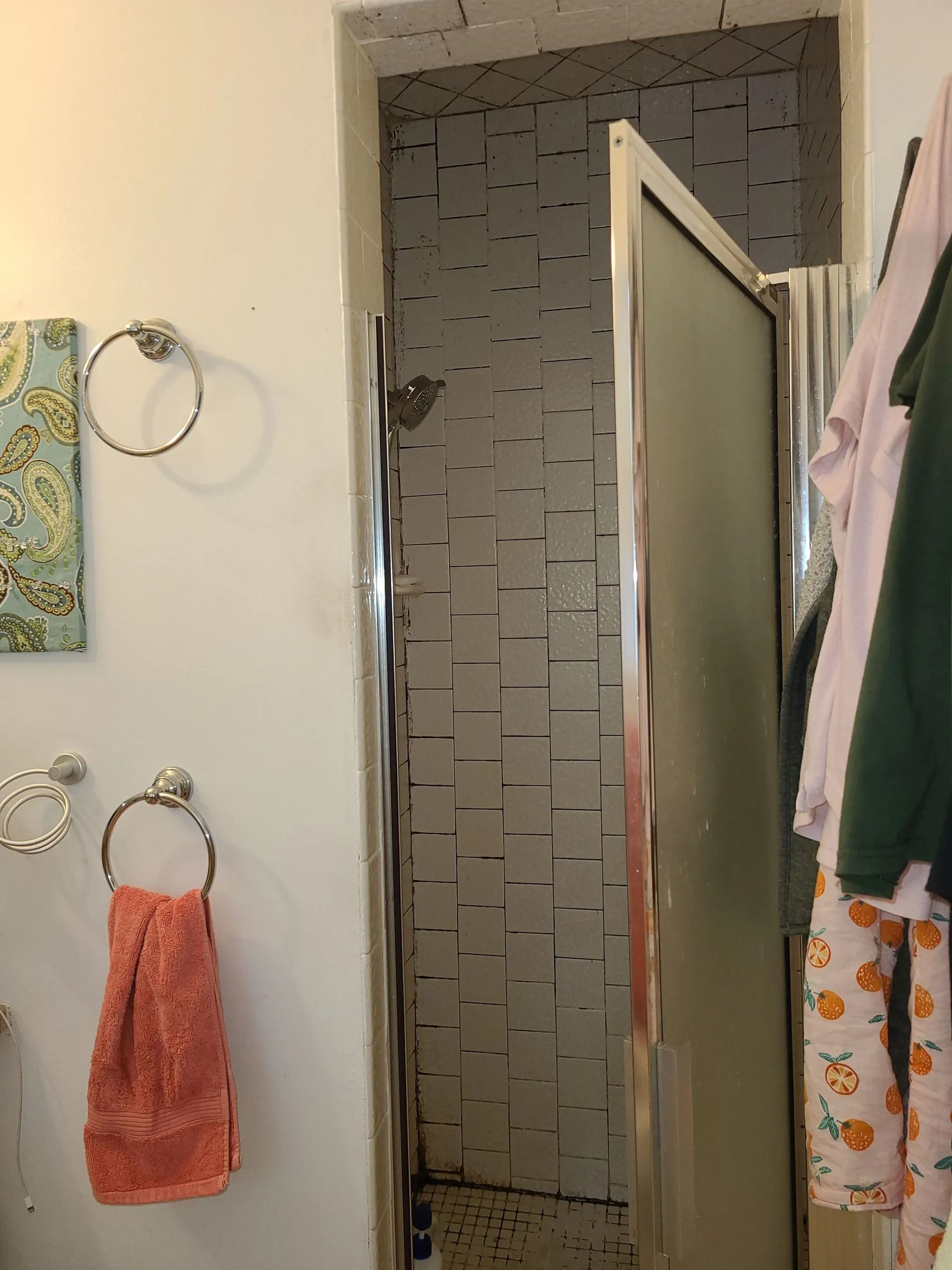 A bathroom with a shower and partially open glass door, white walls, and a towel on a rack.