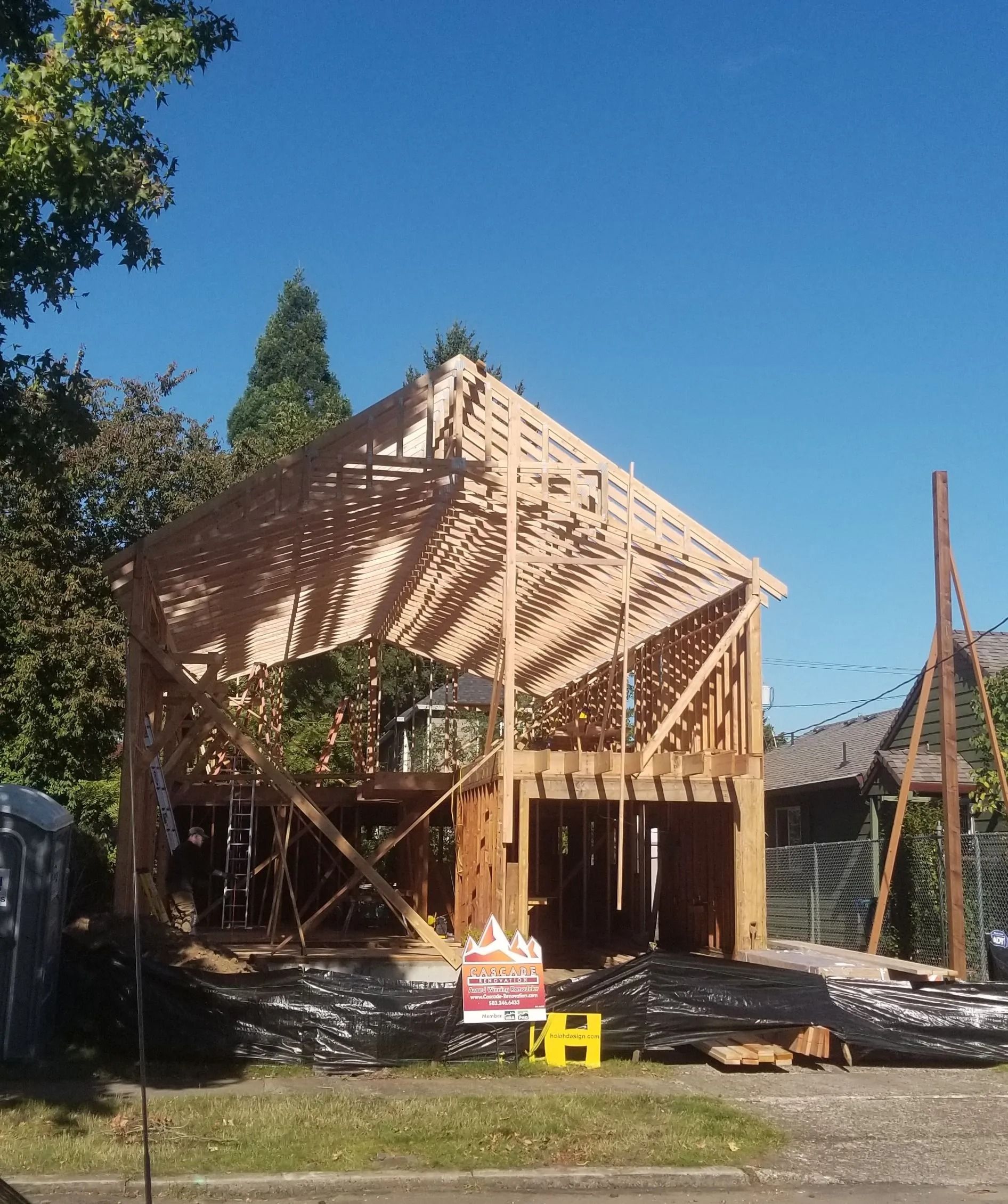 Wooden house under construction with roof framework against a bright blue sky.
