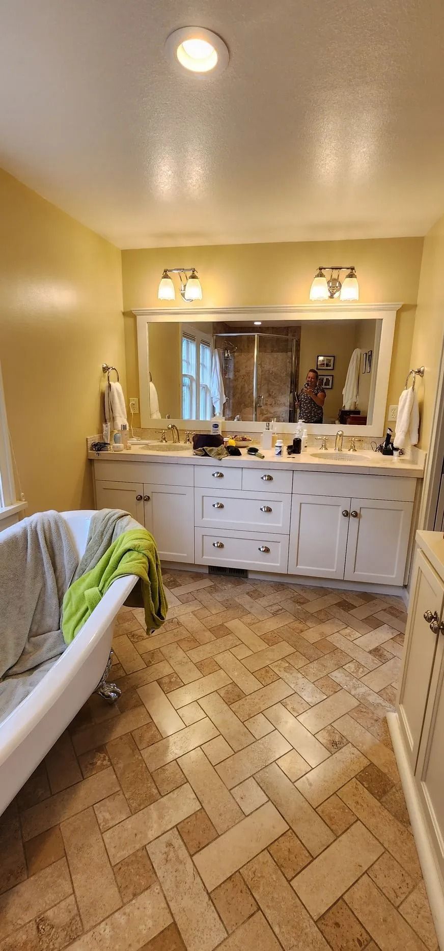 Bathroom with white vanity, large mirror, and clawfoot tub; yellow walls and herringbone tile floor.