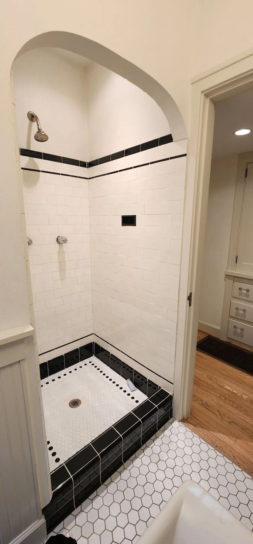 A white tiled shower with black accents and a black tile border, with an arched ceiling.
