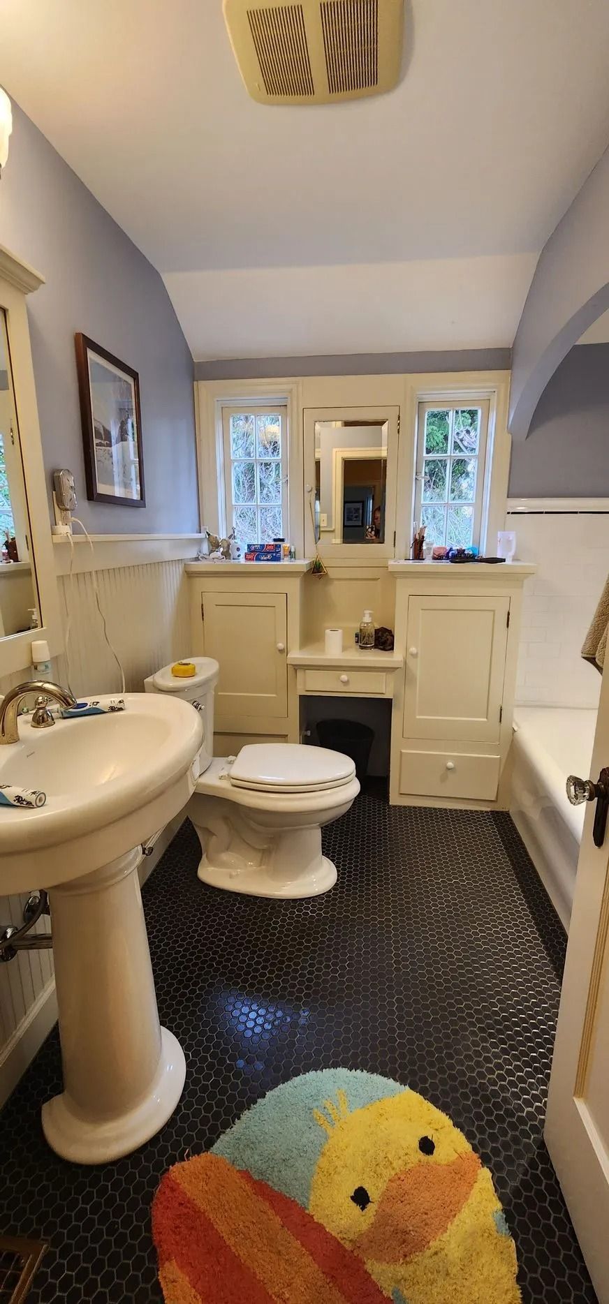 Bathroom with black tiled floor, white fixtures, and a colorful duck rug.