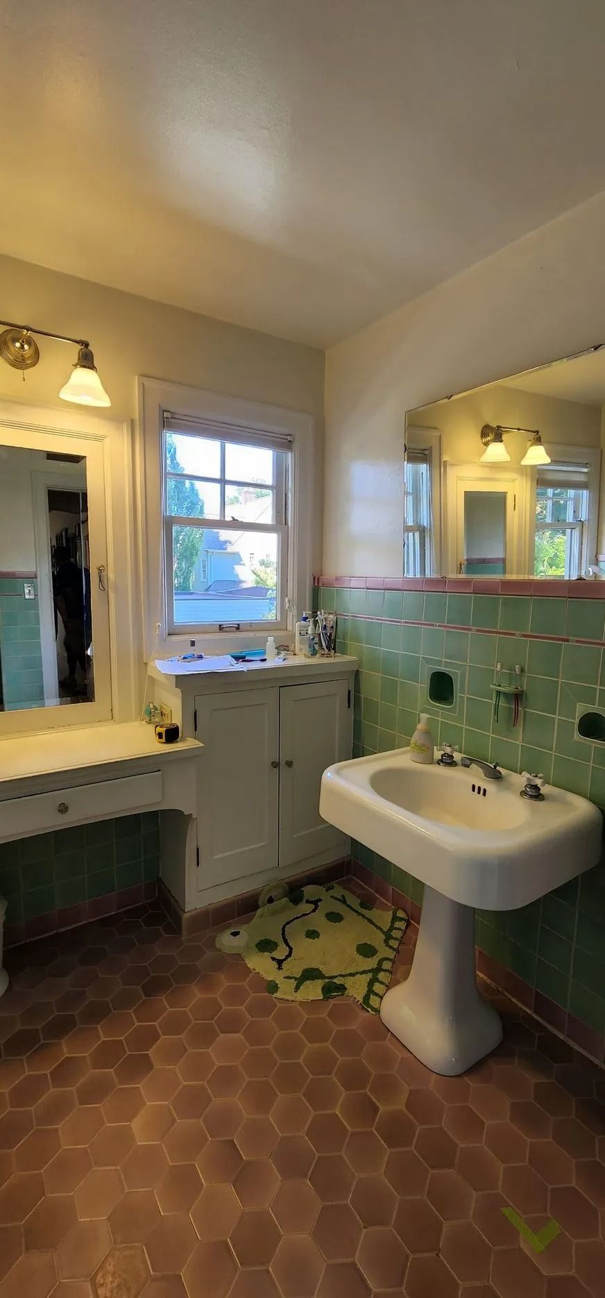 Bathroom with green tile backsplash, pedestal sink, and terracotta hexagon floor tiles.
