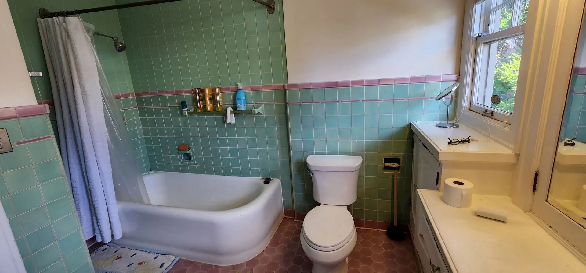 Bathroom with a green tile, white tub, toilet, and vanity with a window.