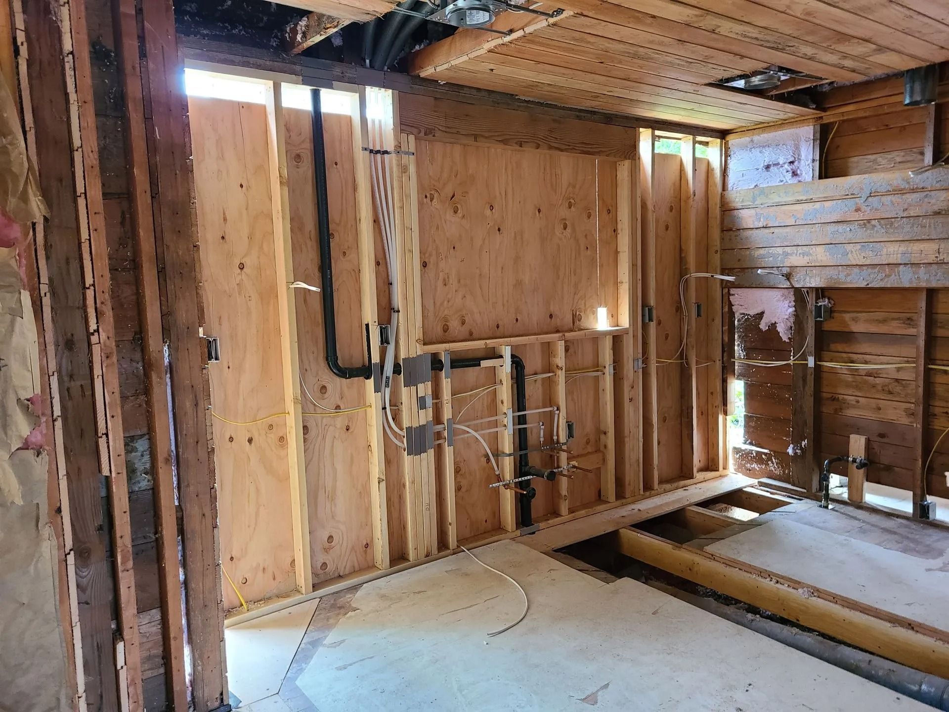 Interior view of a room under construction with exposed plywood walls, plumbing, and open ceiling.