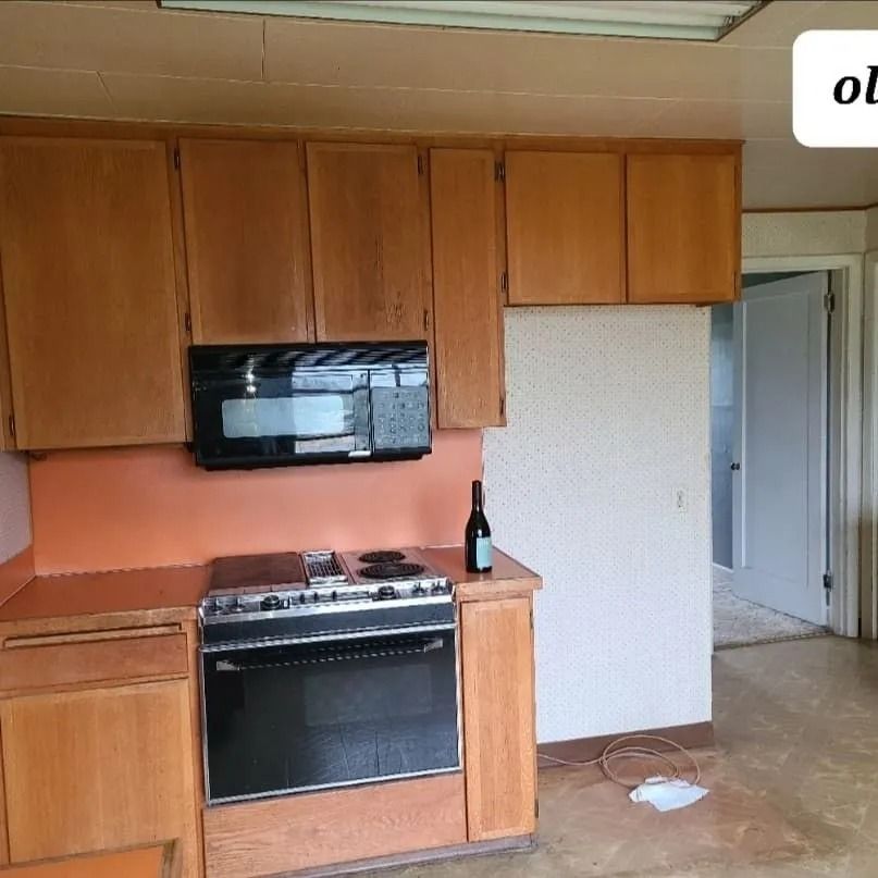 Kitchen with wood cabinets, microwave, stove, and a bottle of wine on counter.