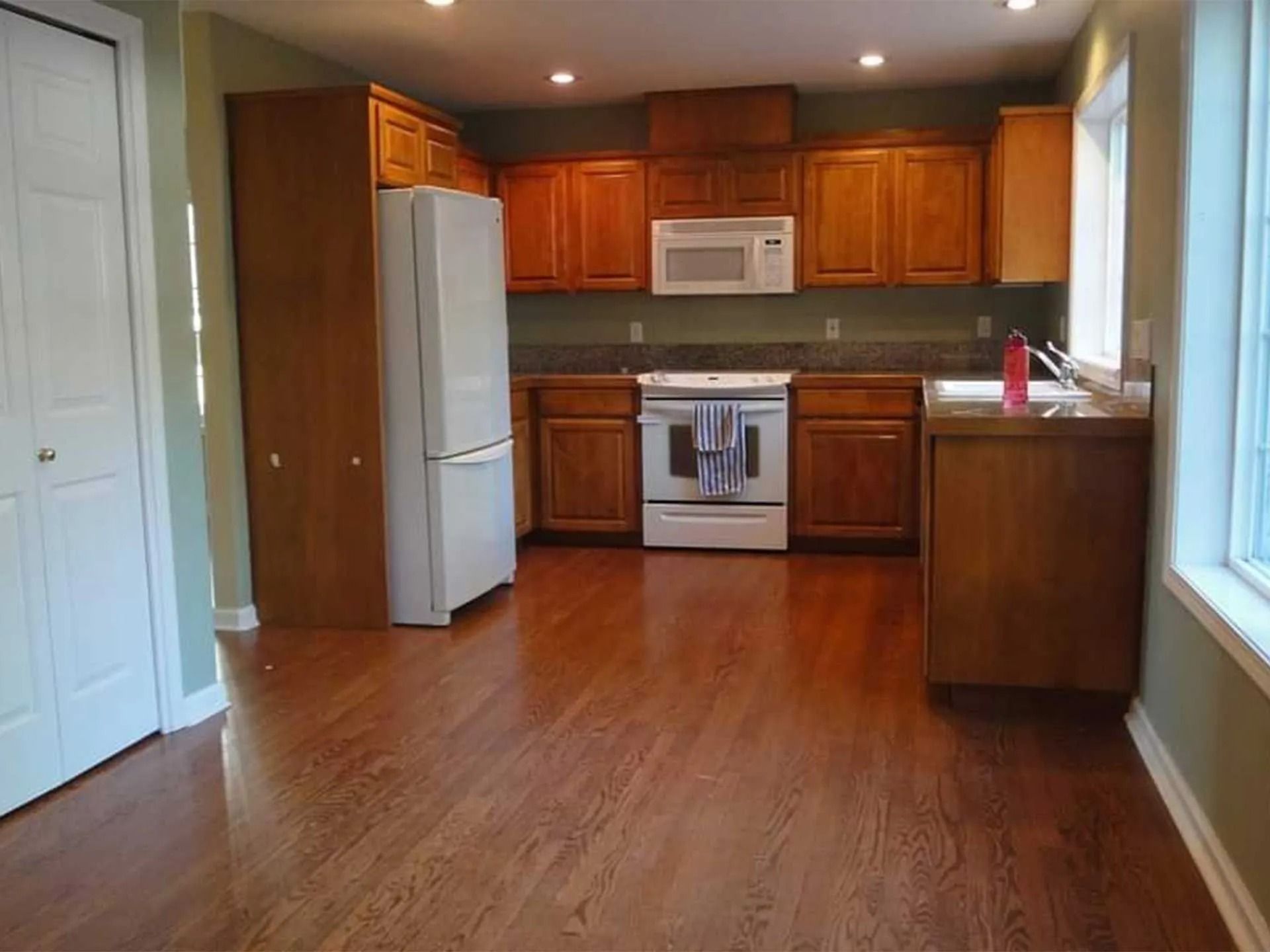 Kitchen with wood cabinets, white appliances, and hardwood floors.