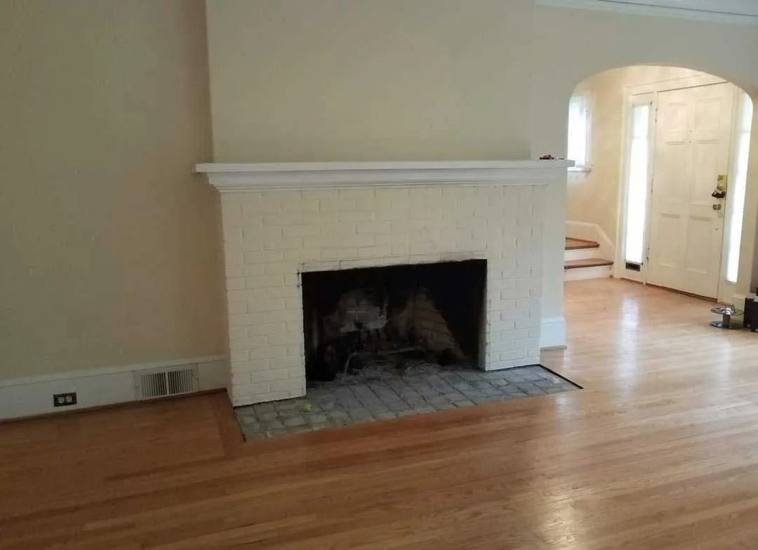 Fireplace in a living room with wooden floors, neutral walls, and arched doorway to the right.