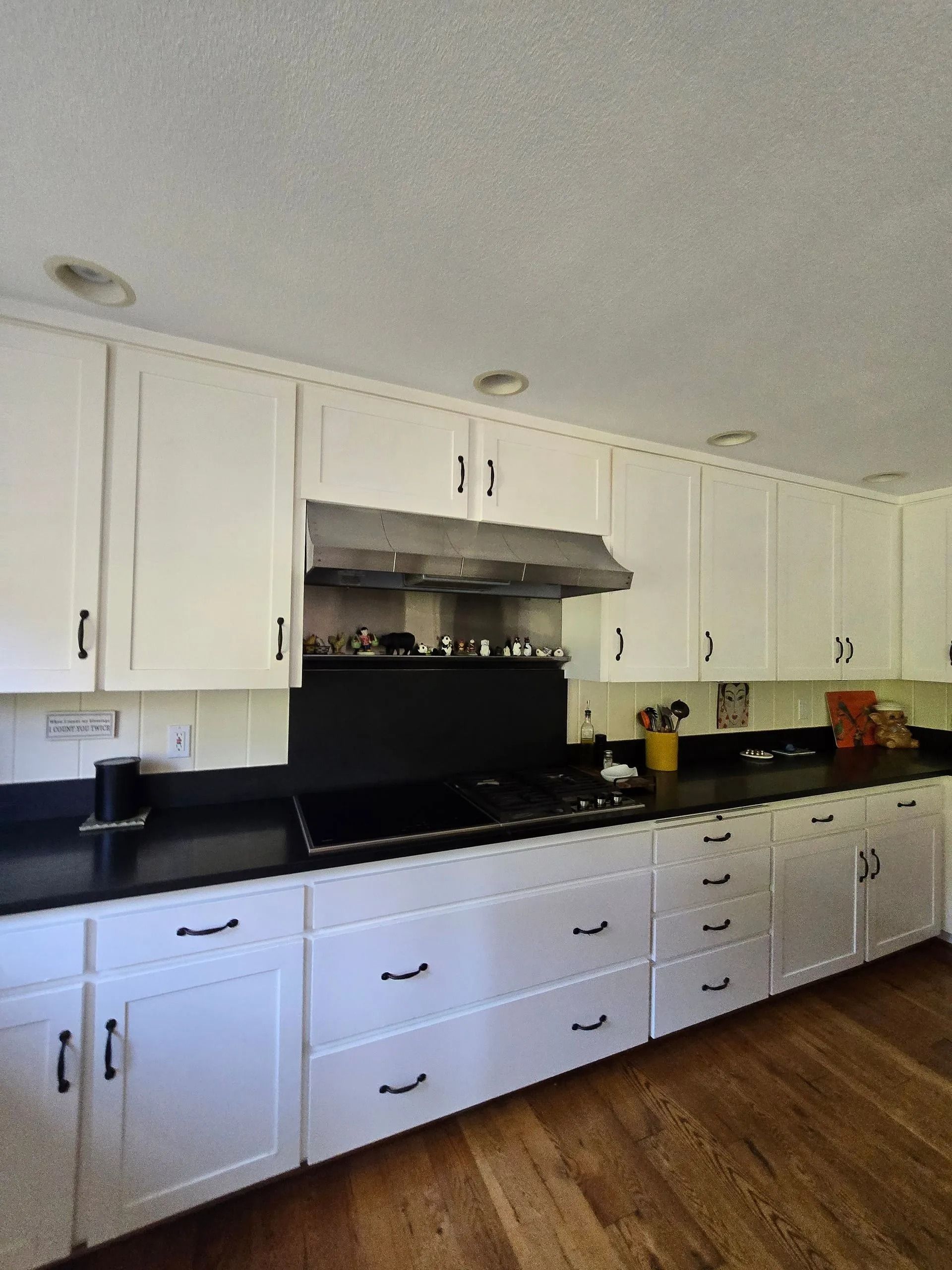 White kitchen cabinets with black countertops and appliances, wooden floor.