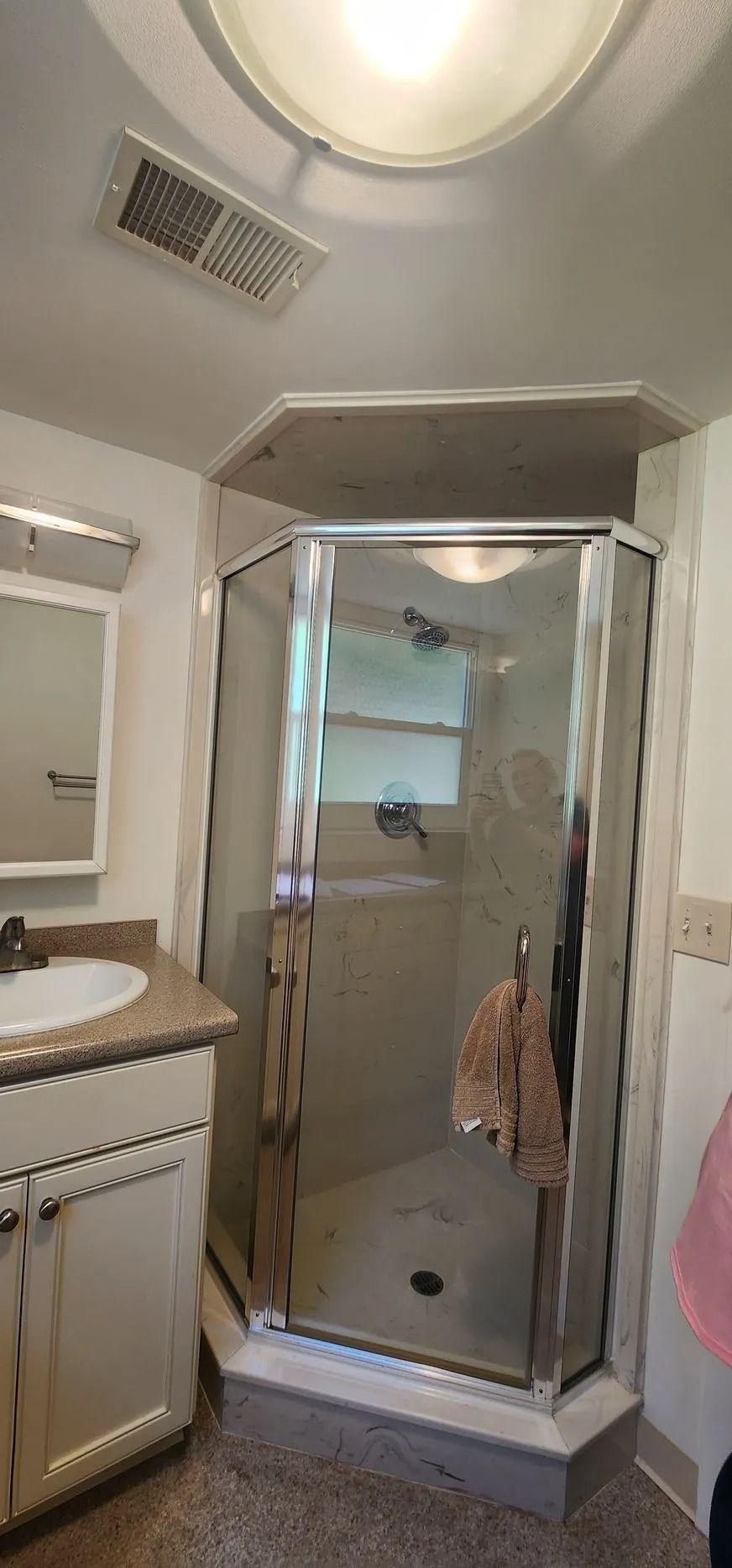 Bathroom with a shower, vanity, and overhead lighting. White cabinets and a light-colored countertop.