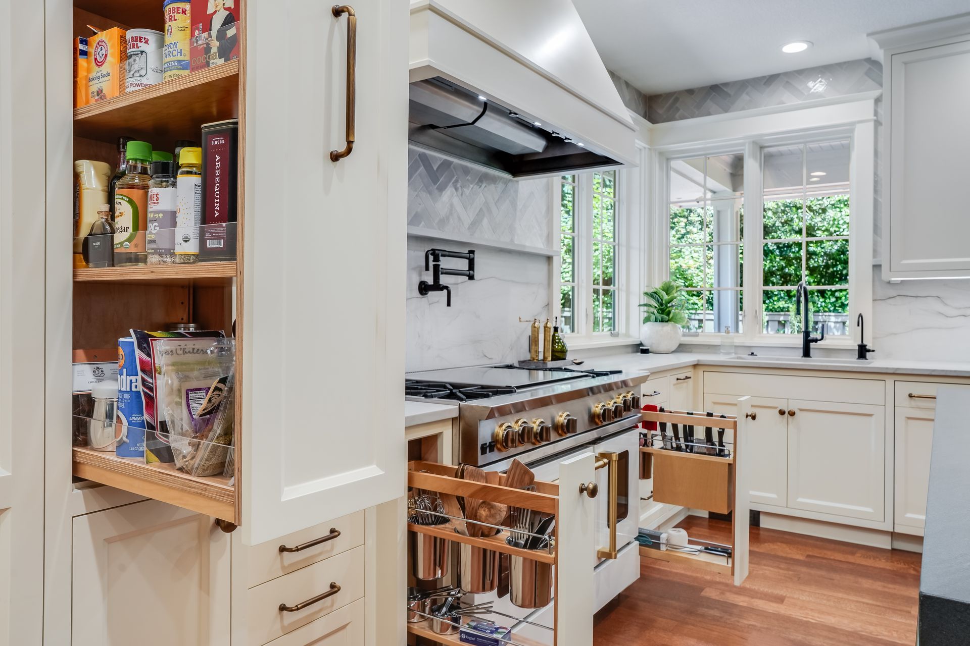 A bright kitchen interior with white cabinets, featuring pull-out spice racks and organized storage drawers.