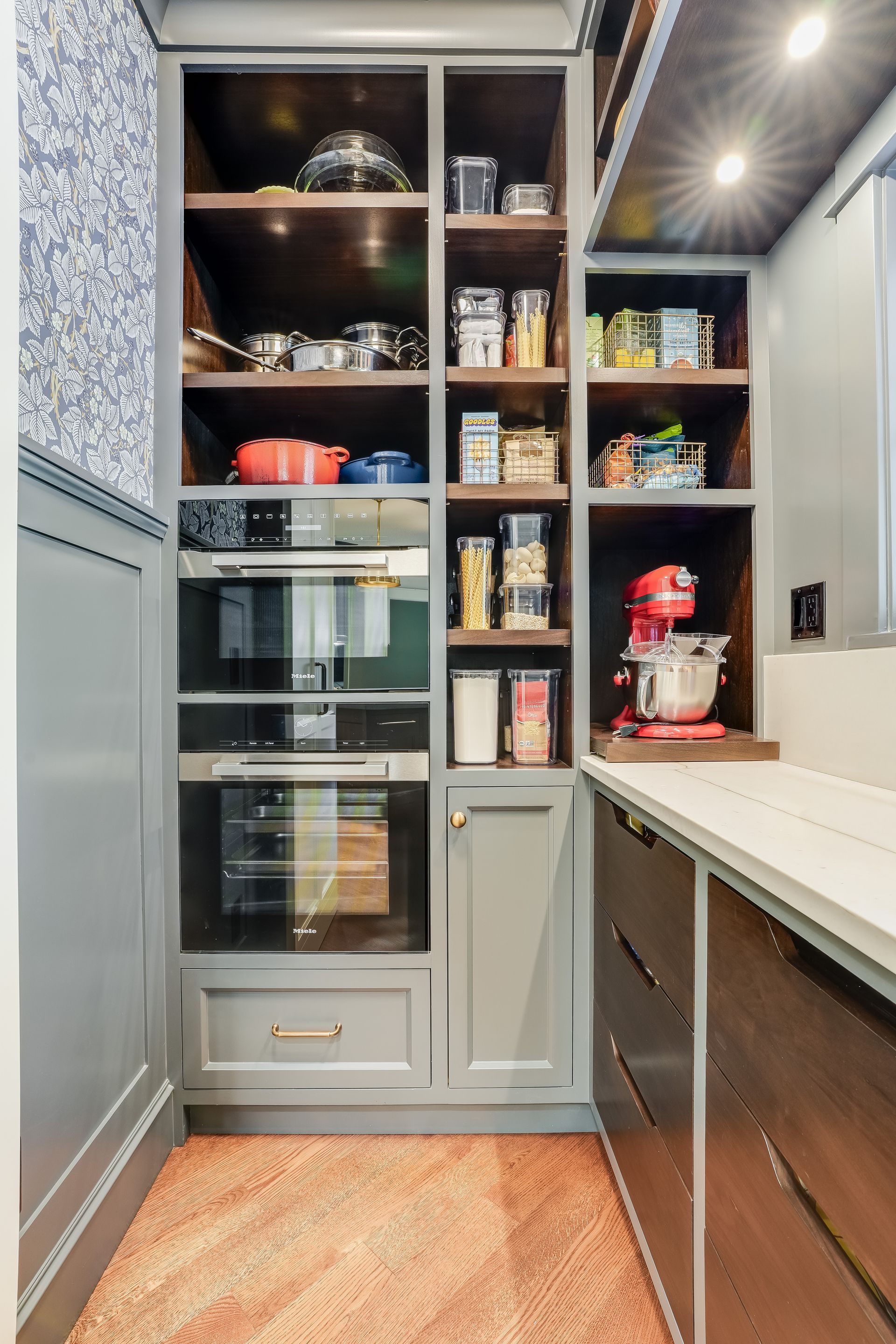 A built-in kitchen pantry featuring open shelves with organized containers, a double oven, and a red stand mixer on a counter.