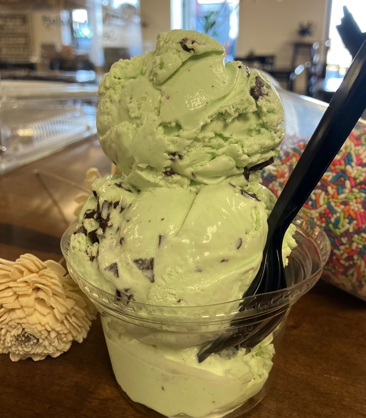 A cup of mint chocolate chip ice cream with a spoon in it.