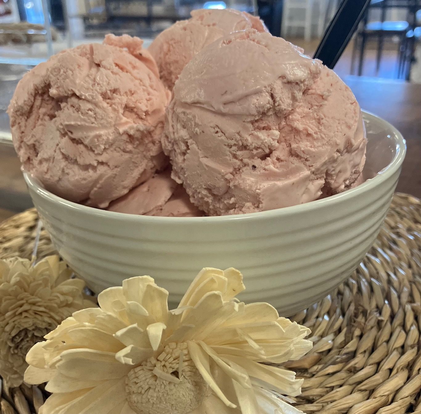 A white bowl filled with pink ice cream next to a flower