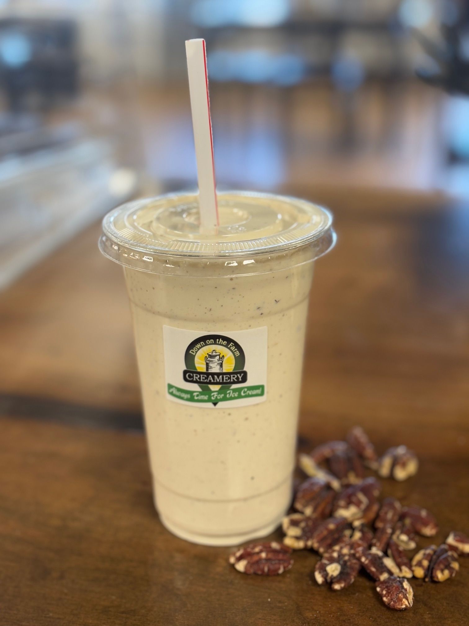 A smoothie with a straw in it is sitting on a wooden table next to pecans.