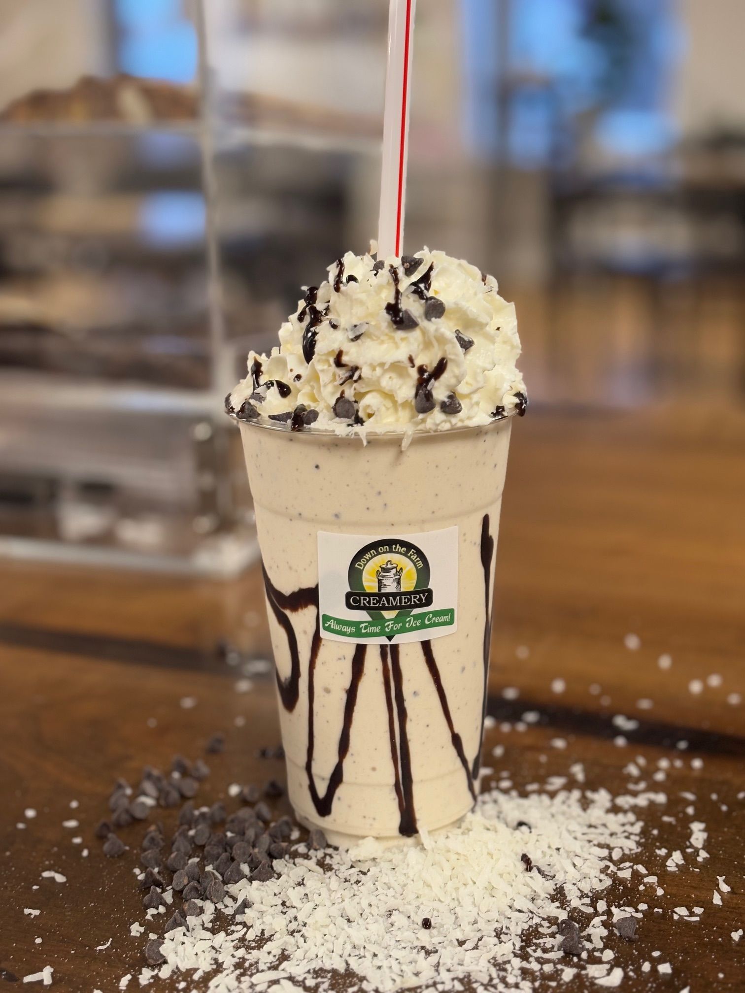 A milkshake with whipped cream and chocolate chips in a cup with a straw.