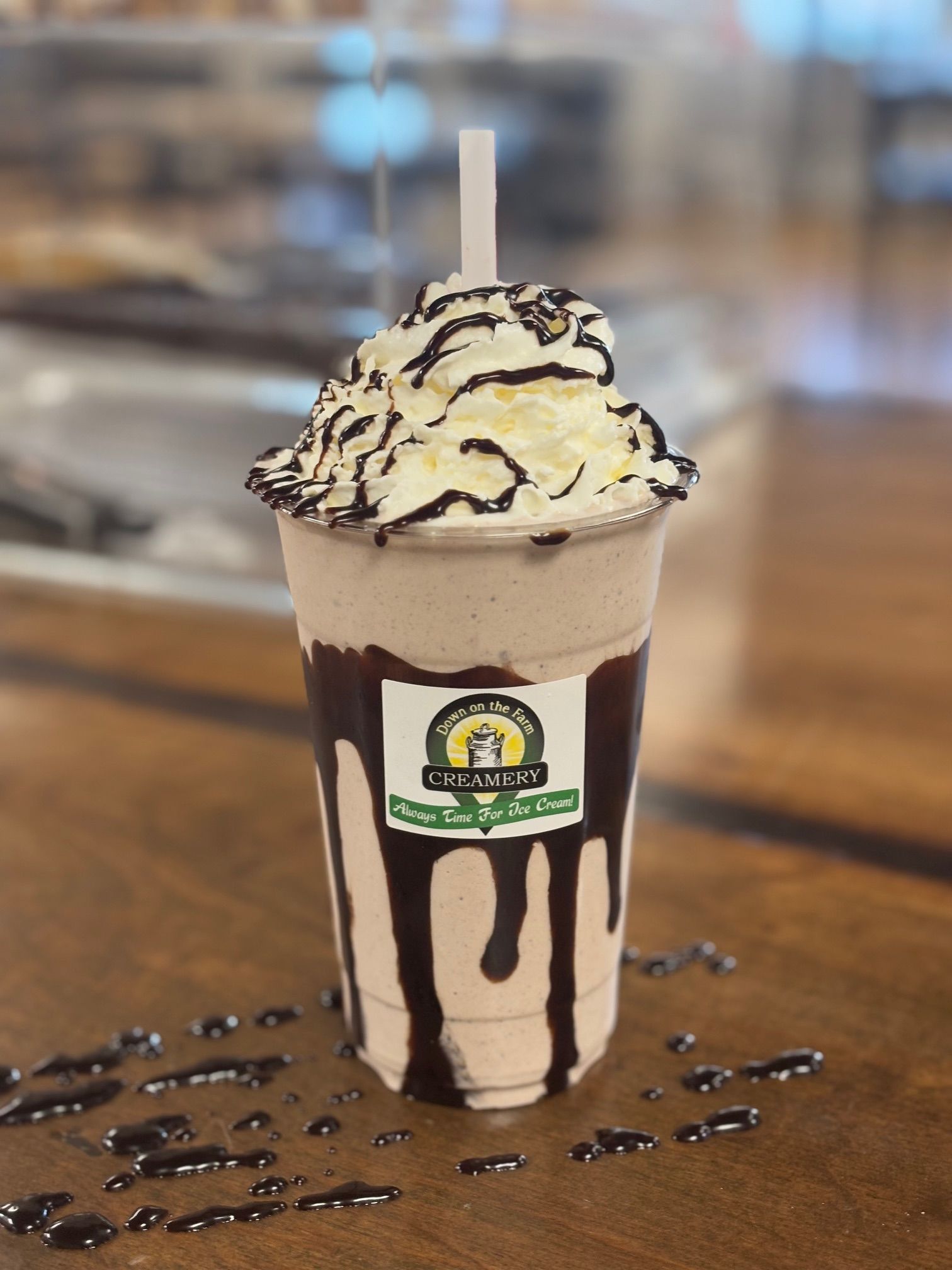 A milkshake with whipped cream and chocolate sauce is sitting on a wooden table.