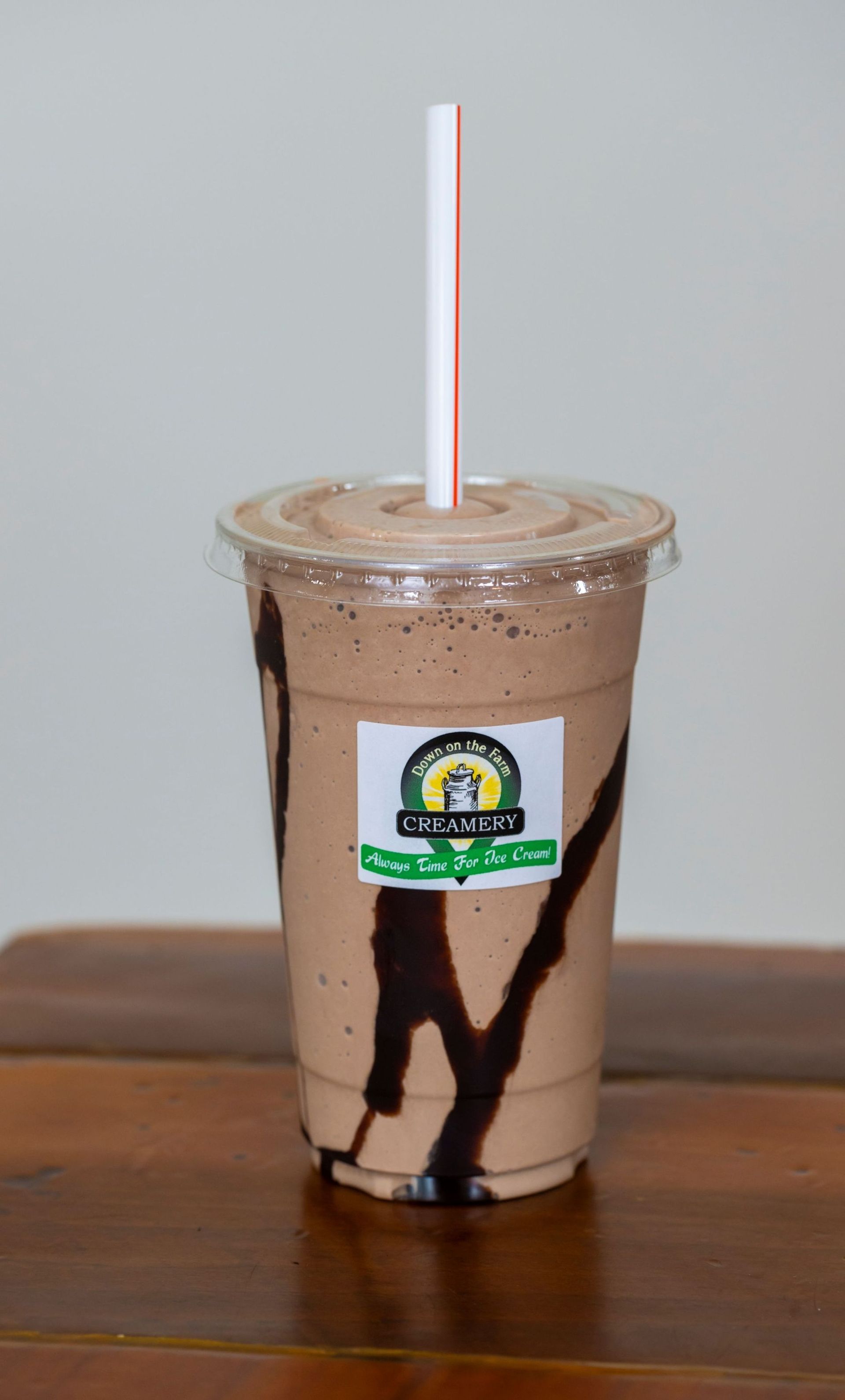 A chocolate milkshake with a straw in it is sitting on a wooden table.