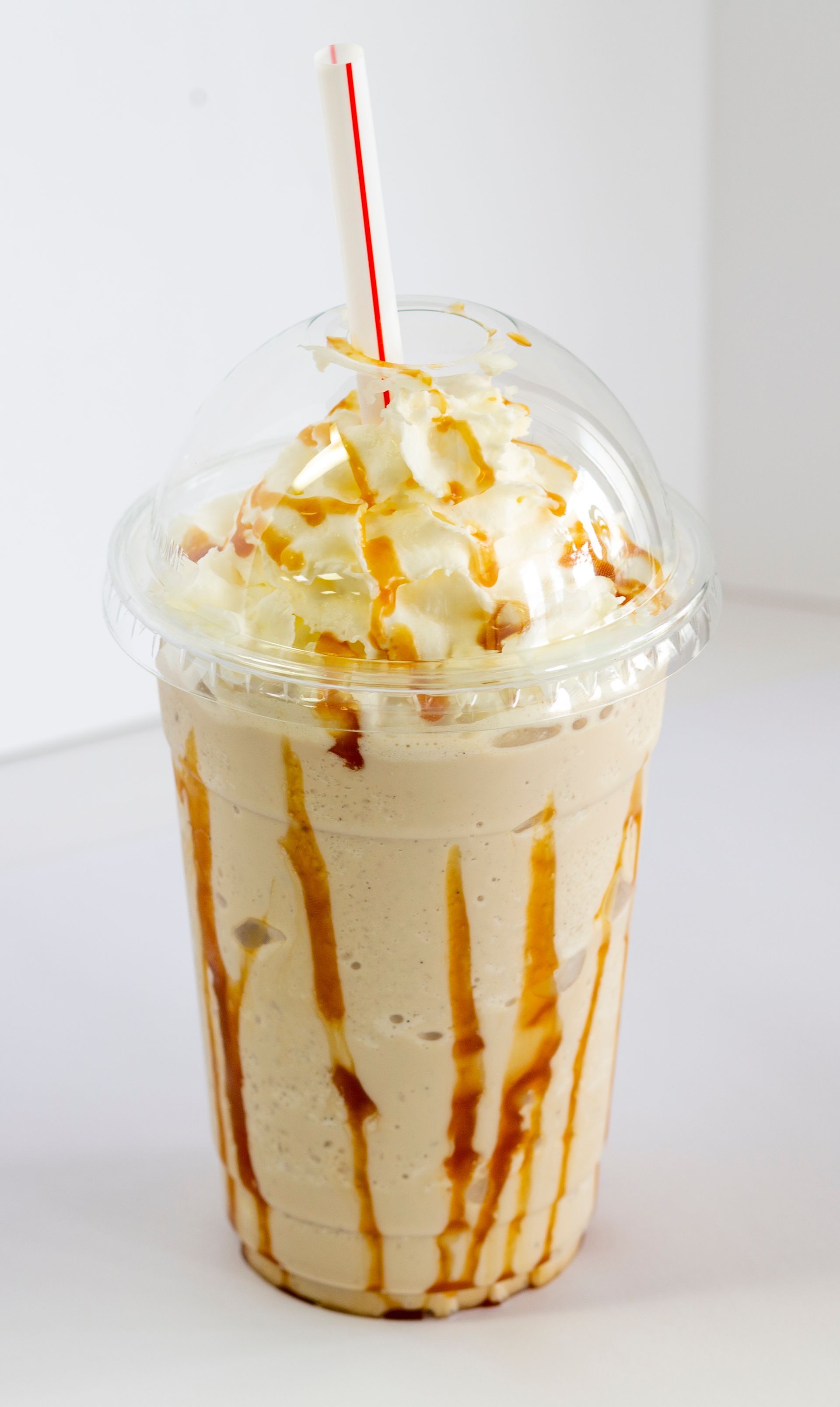 A milkshake with whipped cream and caramel sauce in a plastic cup with a straw.