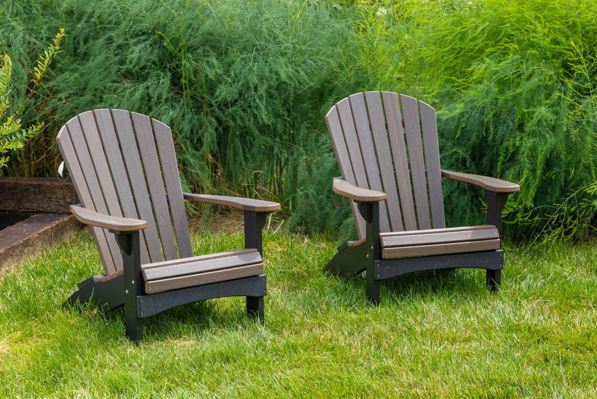 Two adirondack chairs are sitting on top of a lush green lawn.