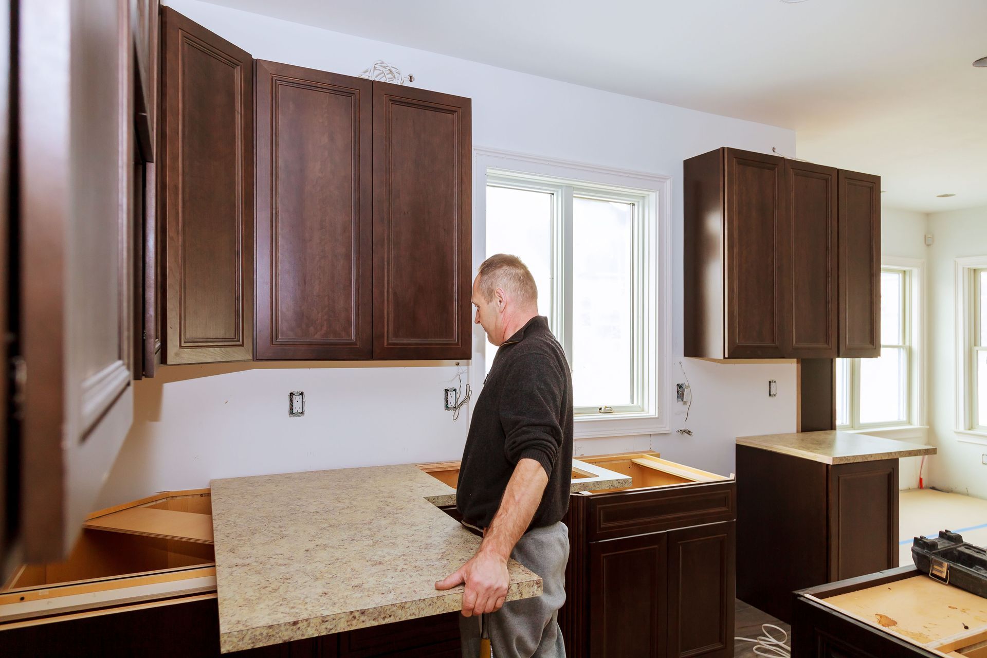 Man installing a granite countertop in a kitchen with dark brown cabinets.