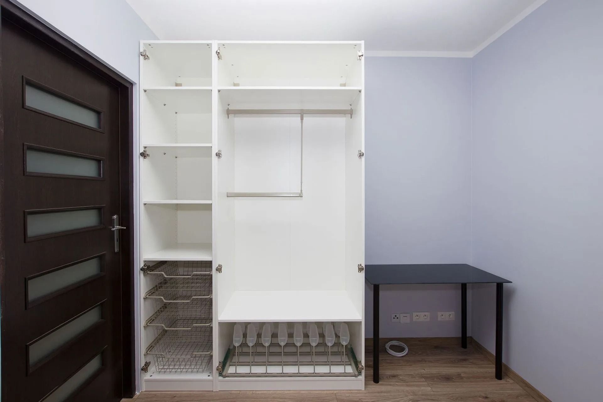 White open closet next to a dark door and black table in a room with light purple walls.